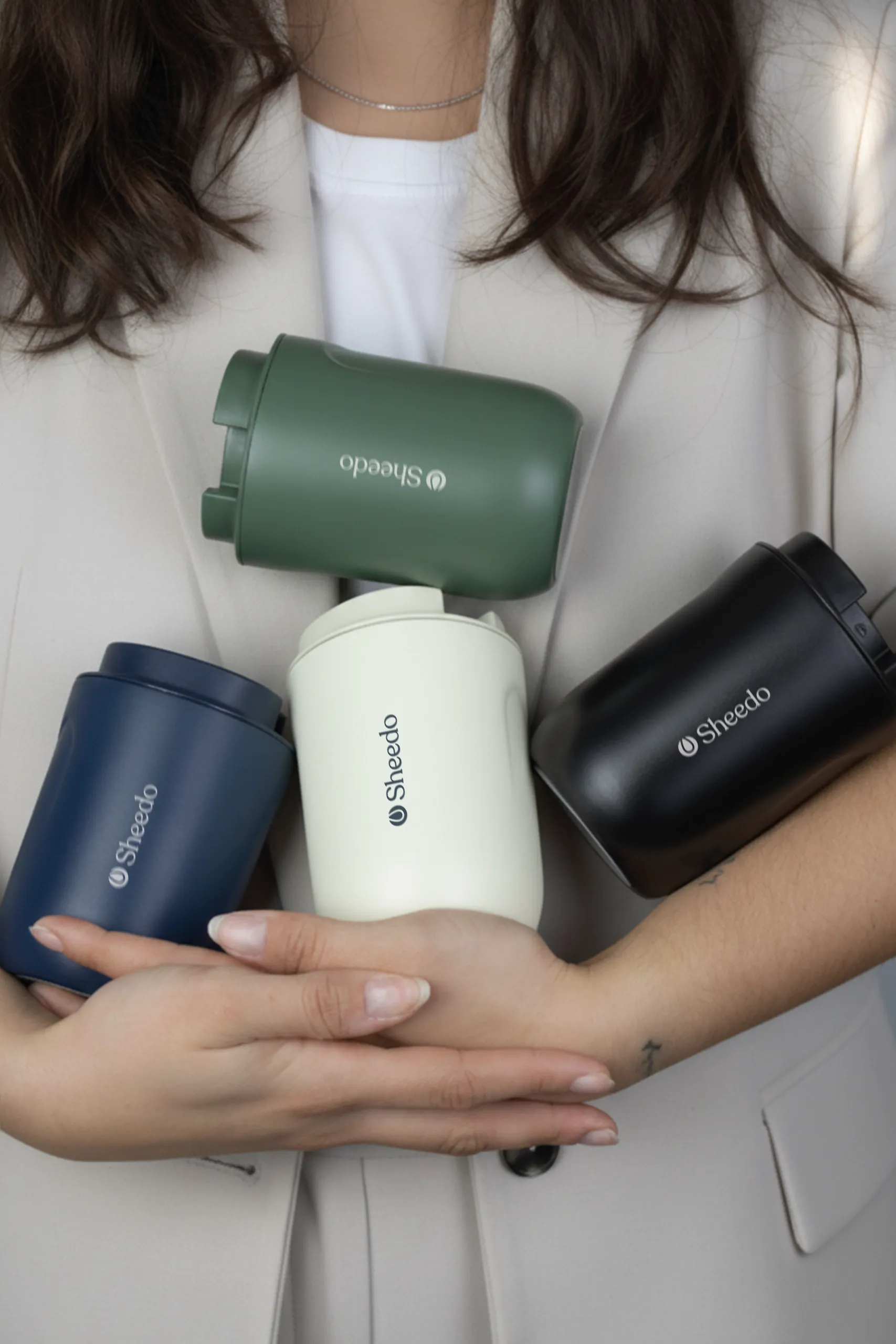 Chica sosteniendo en sus brazos 4 vasos térmicos personalizados con el logotipo de 'Sheedo'