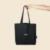 Mano sujetando una bolsa negra de algodón reciclado personalizada con logo de color blanco.