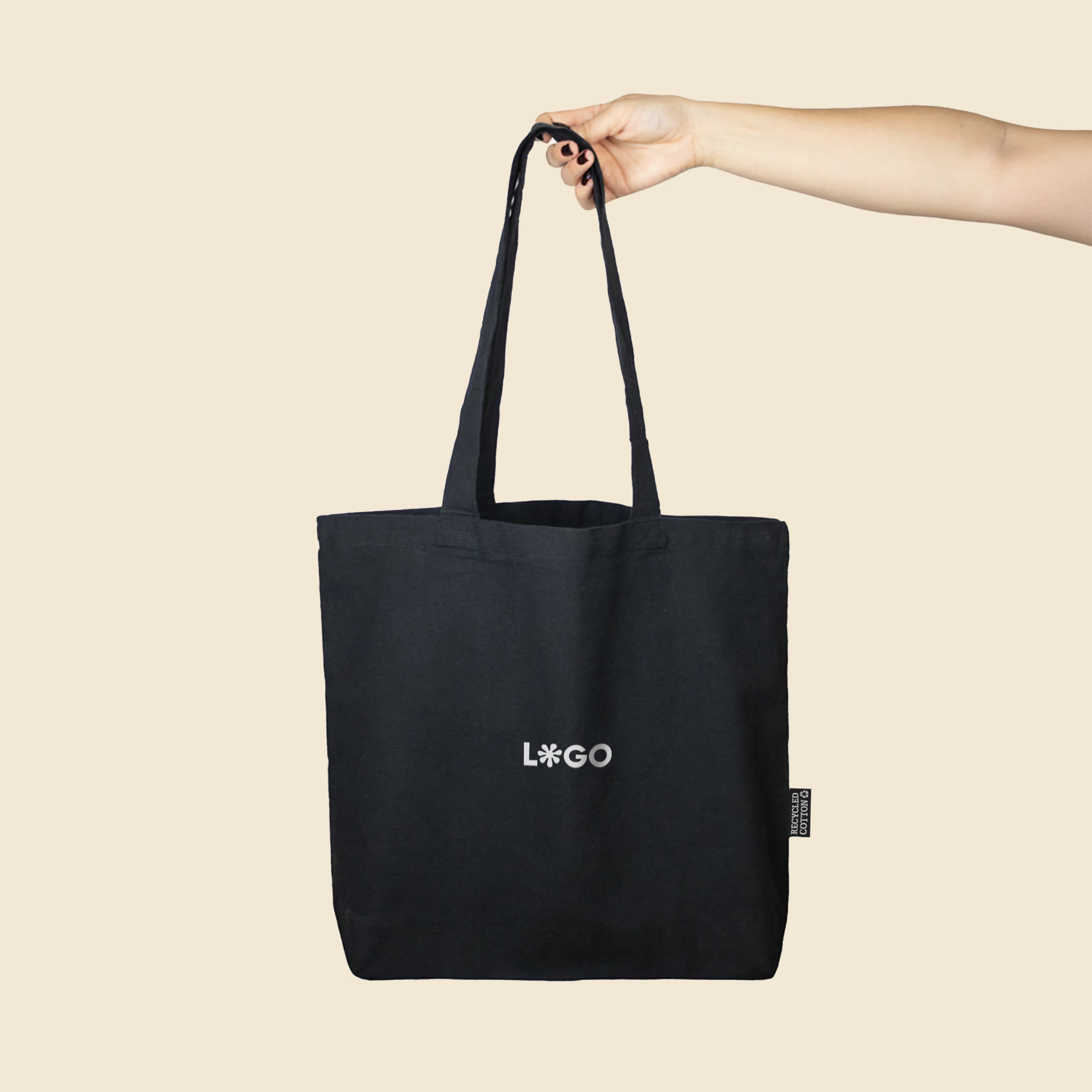 Mano sujetando una bolsa negra de algodón reciclado personalizada con logo de color blanco.