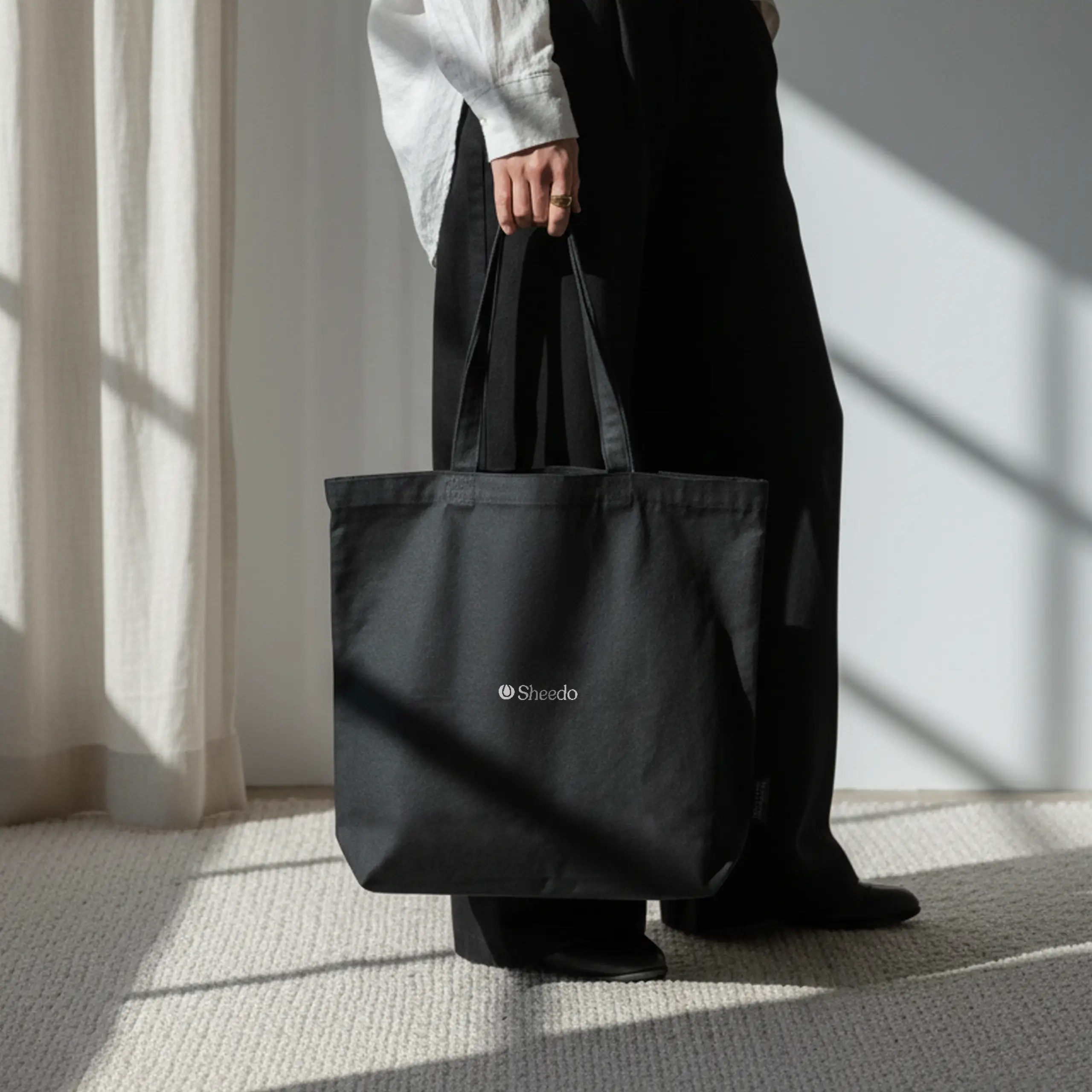 Persona en una habitación llevando una bolsa negra de algodón reciclado personalizada con logo blanco.