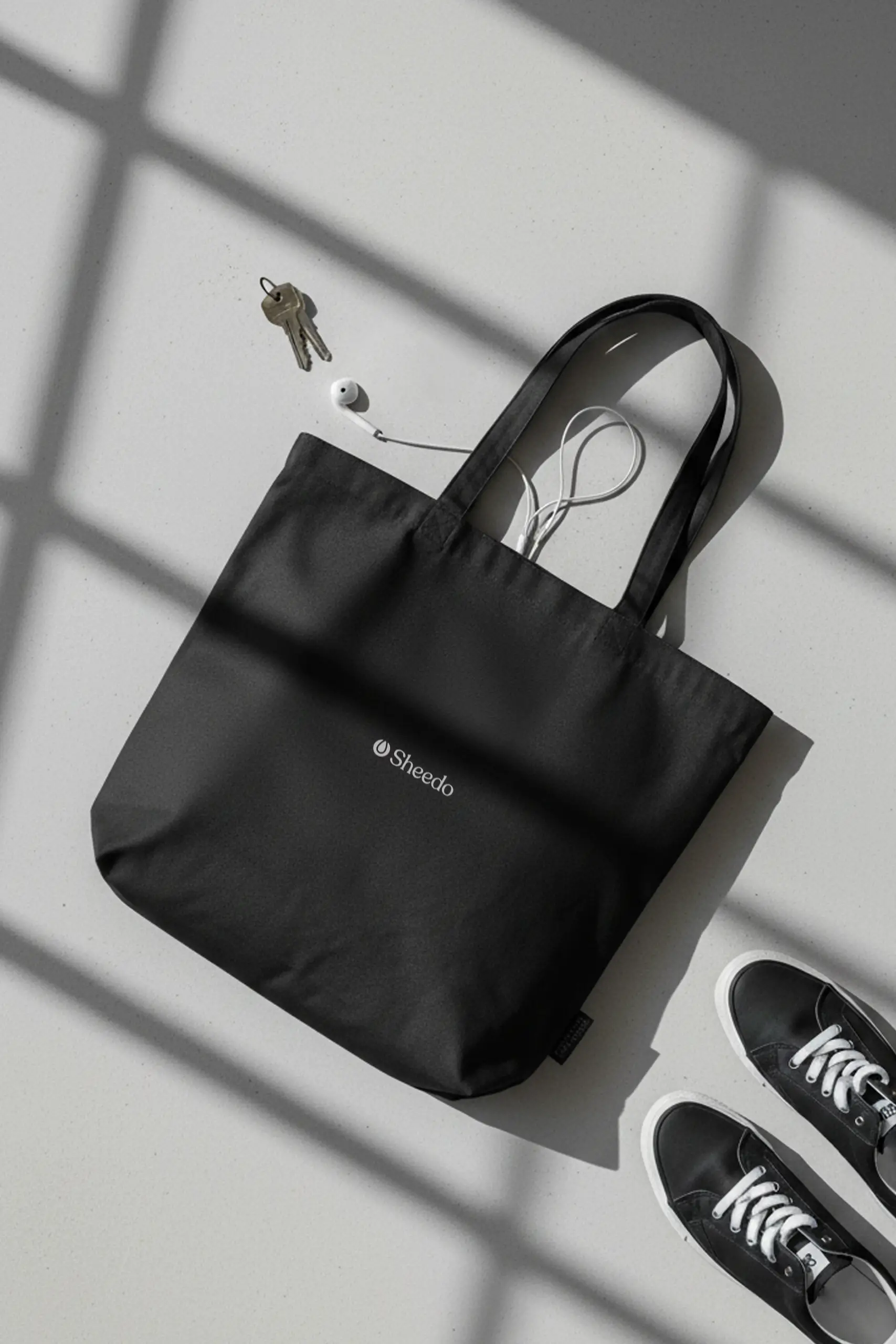 Bolsa de algodón negra personalizada en color blanco colocada en el suelo juntos a una zapatillas en una habitación.