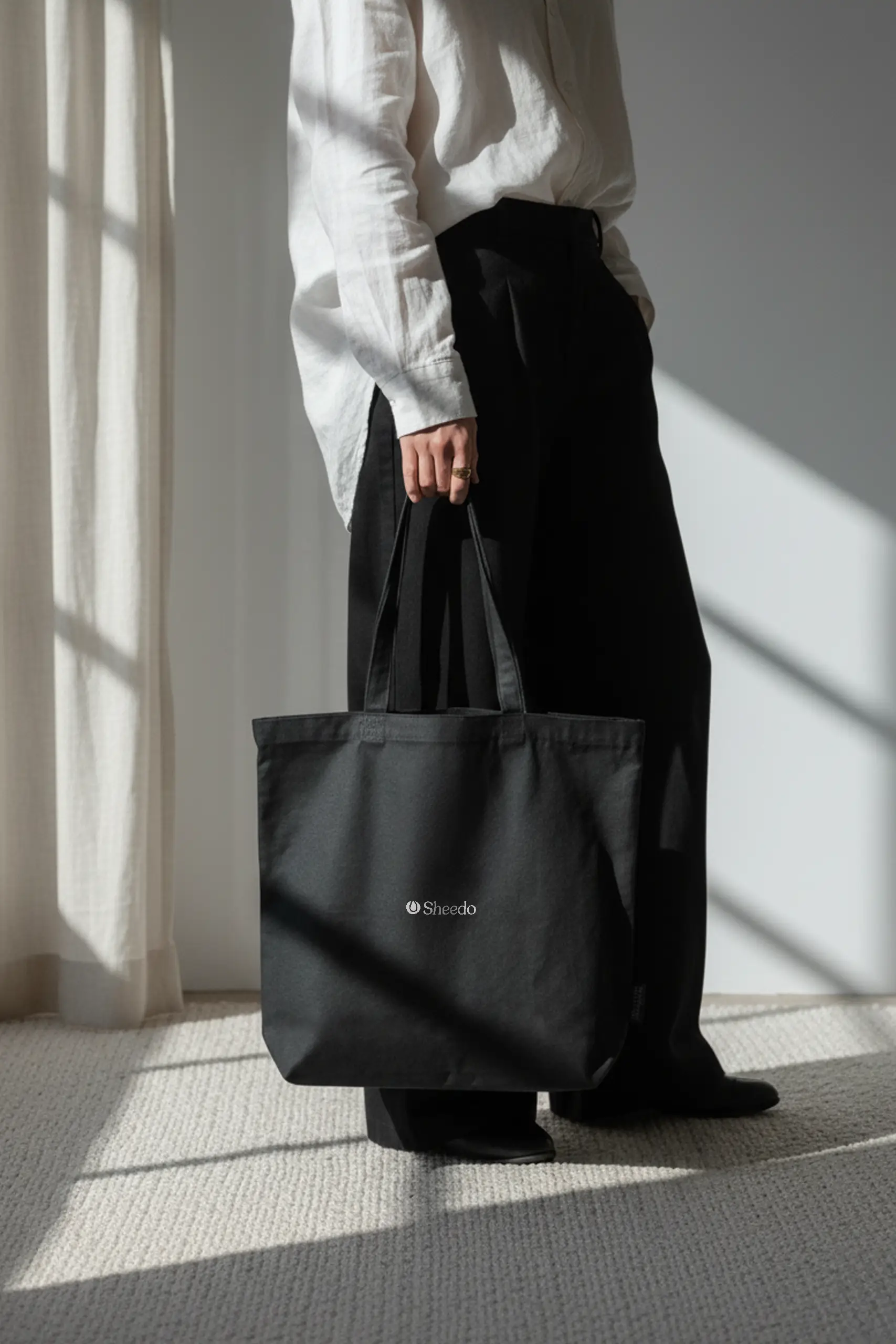 Persona en una sala llevando una bolsa negra de algodón reciclado personalizada con logo blanco.