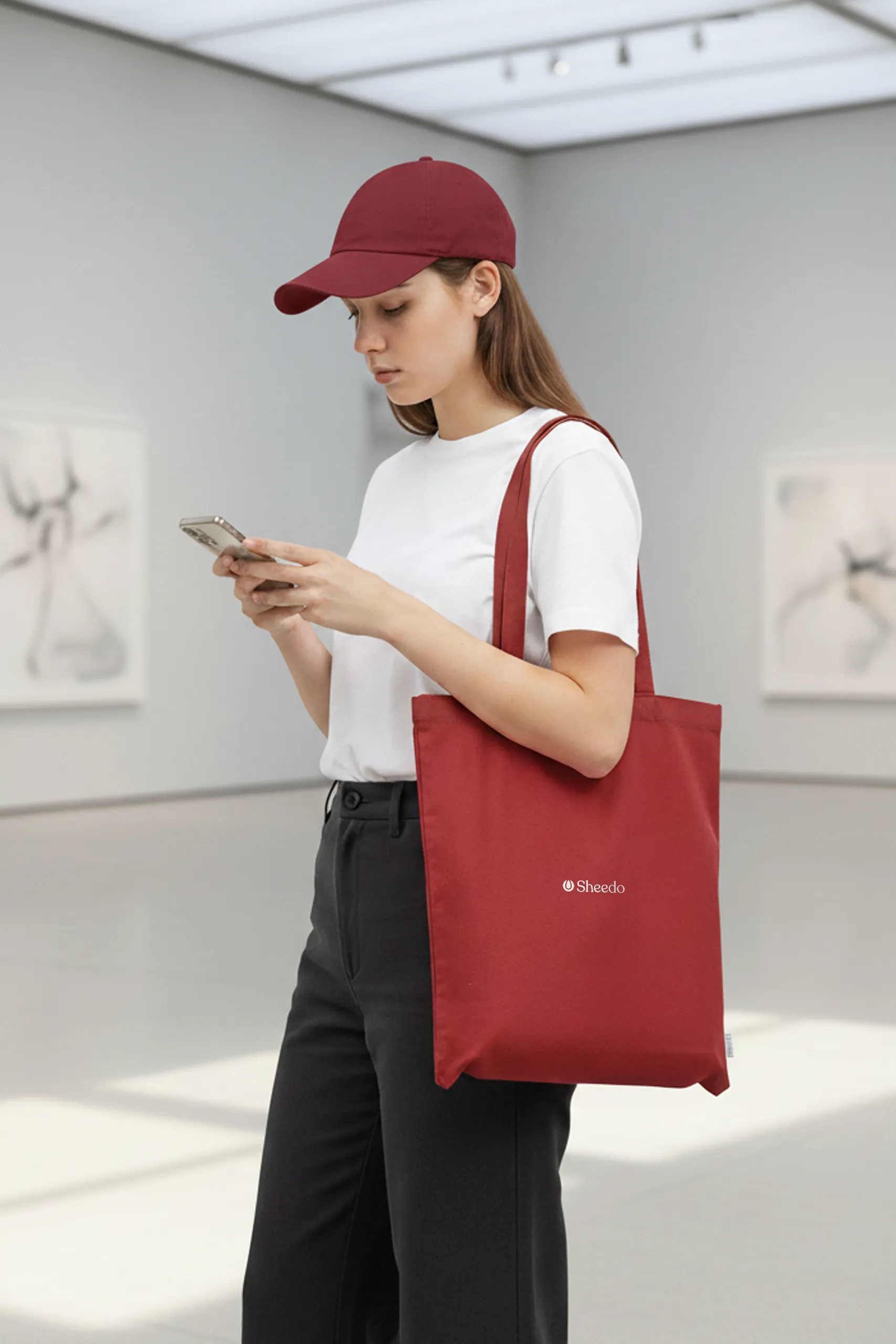 Chica en un museo con una bolsa de algodón reciclado de color rojo con la palabra LOGO en blanco.
