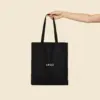 Bolsa de algodón reciclado de color negro con la palabra LOGO en blanco sujetado por una persona.