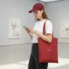 Chica en un museo con una bolsa de algodón reciclado de color rojo con la palabra LOGO en blanco.
