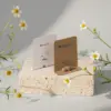 Dos cápsula biodegradables con semillas en su interior con packaging de cartón kraft y blanco personalizado, colocadas sobre una piedra con margaritas alrededor