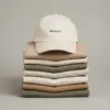 Gorra ecológica algodón orgánico GORKA Gorra ecológica de algodón de color beige personalizada con la palabra 'logo' en marrón, colocada sobre jerseys apilados