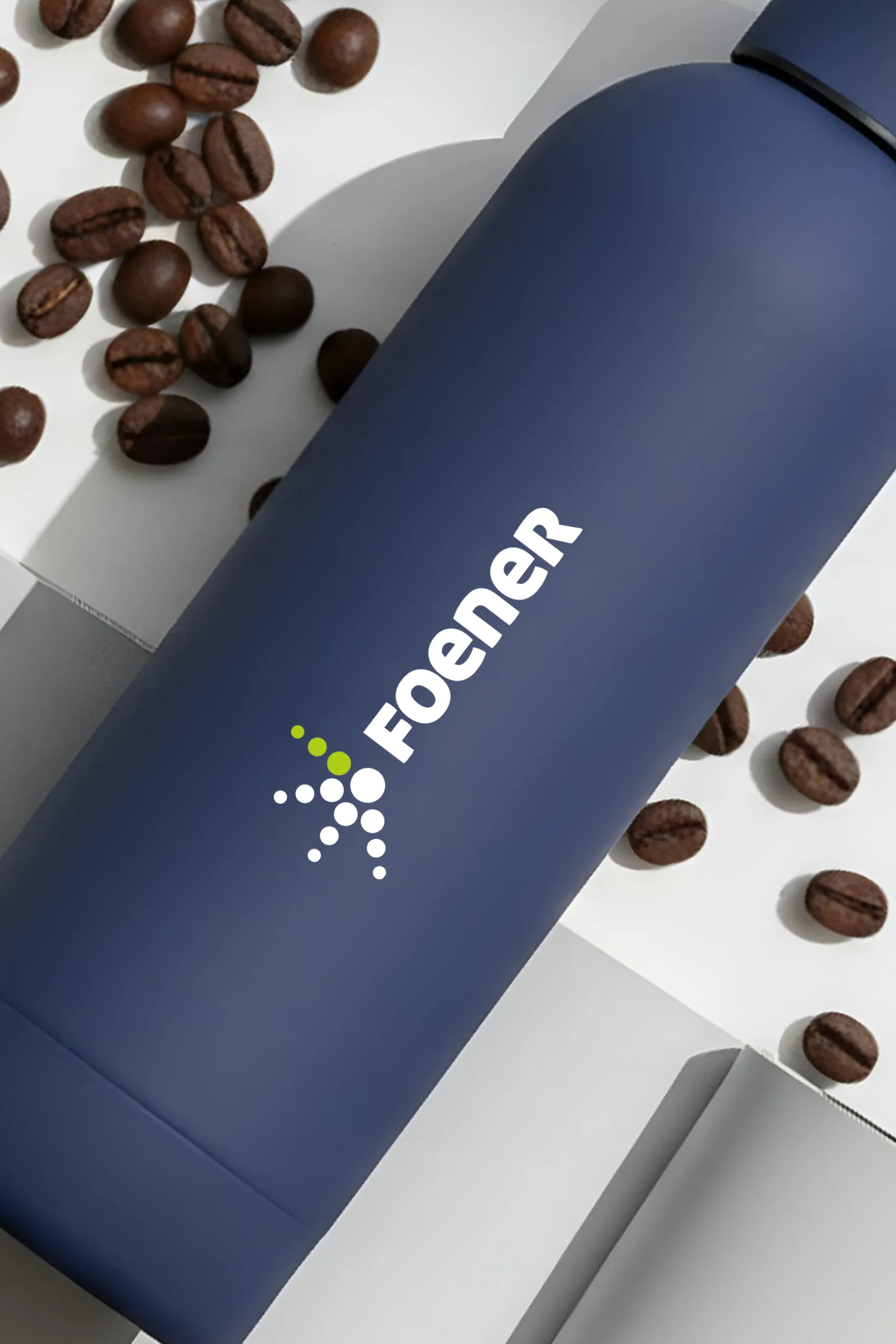 Botella térmica azul personalizada para la marca FOENER, encima de una revista abierta y granos de café