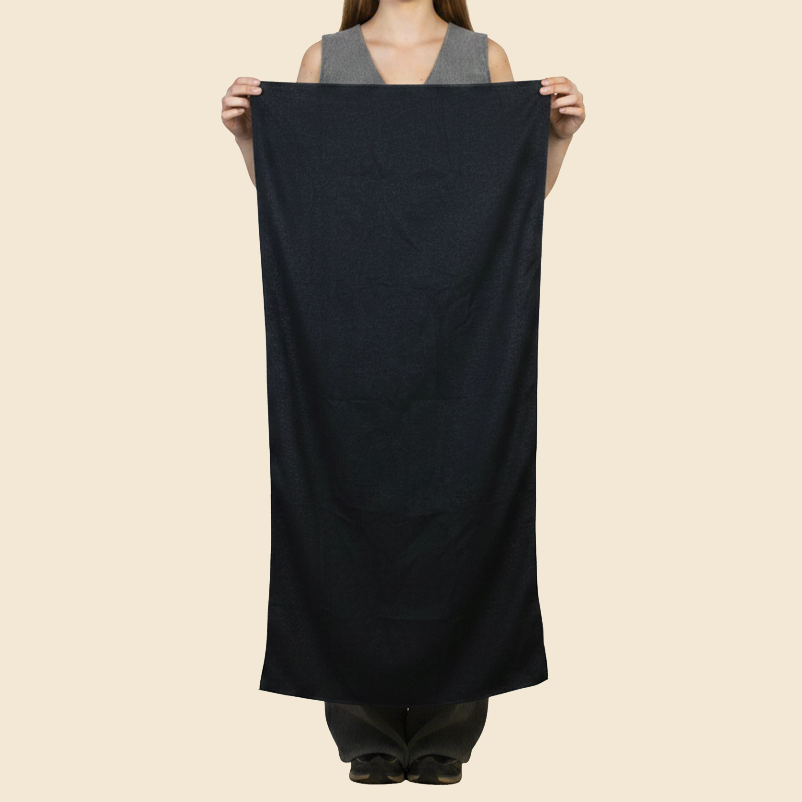 Toalla personalizada de gimnasio, de color negro y de material rpet. Sujeta por una persona y extendida completa.