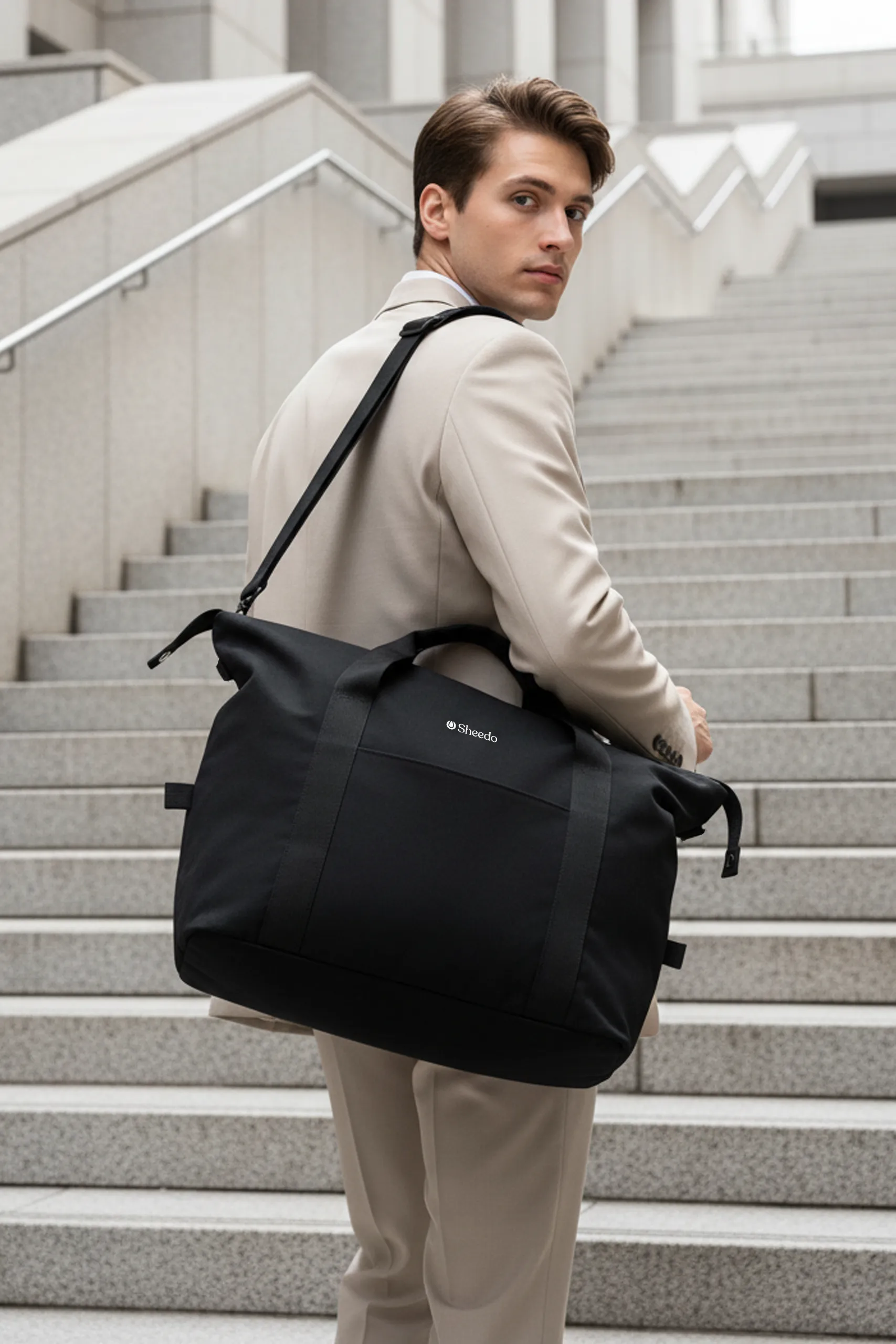 Chico subiendo unas escaleras llevando una bolsa de viaje negra personalizada con el logo de Sheedo en blanco