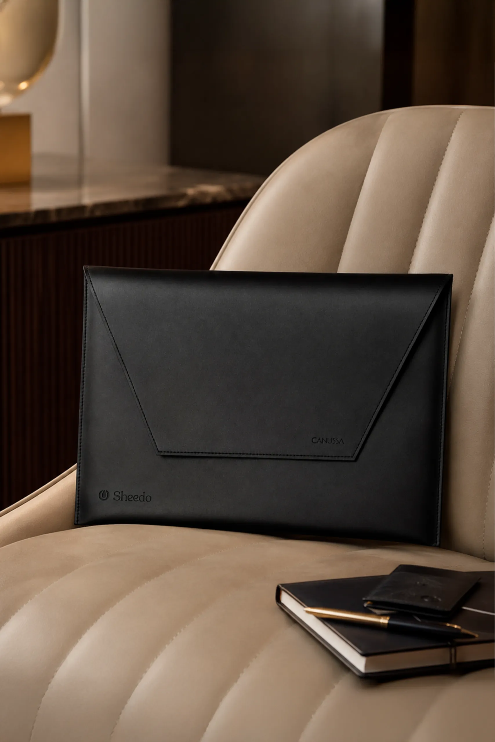 Persona en oficina con una funda de portátil fabricada de residuo de maíz . De color negro y con personalización en grabado láser. Colocado en un sillón de cuero beige.