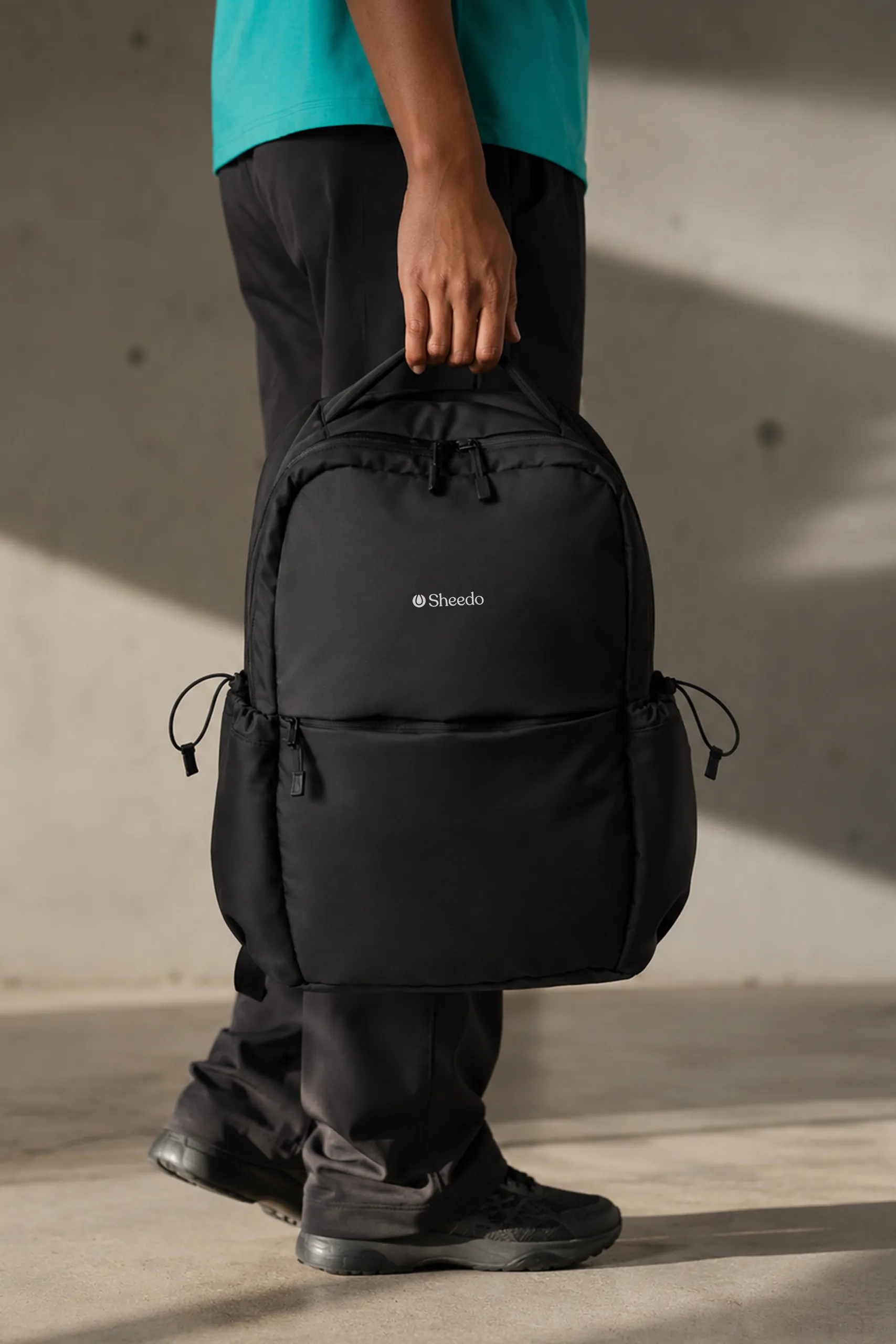 Chica sujetando por el asa una mochila urbana personalizada negra en un exterior