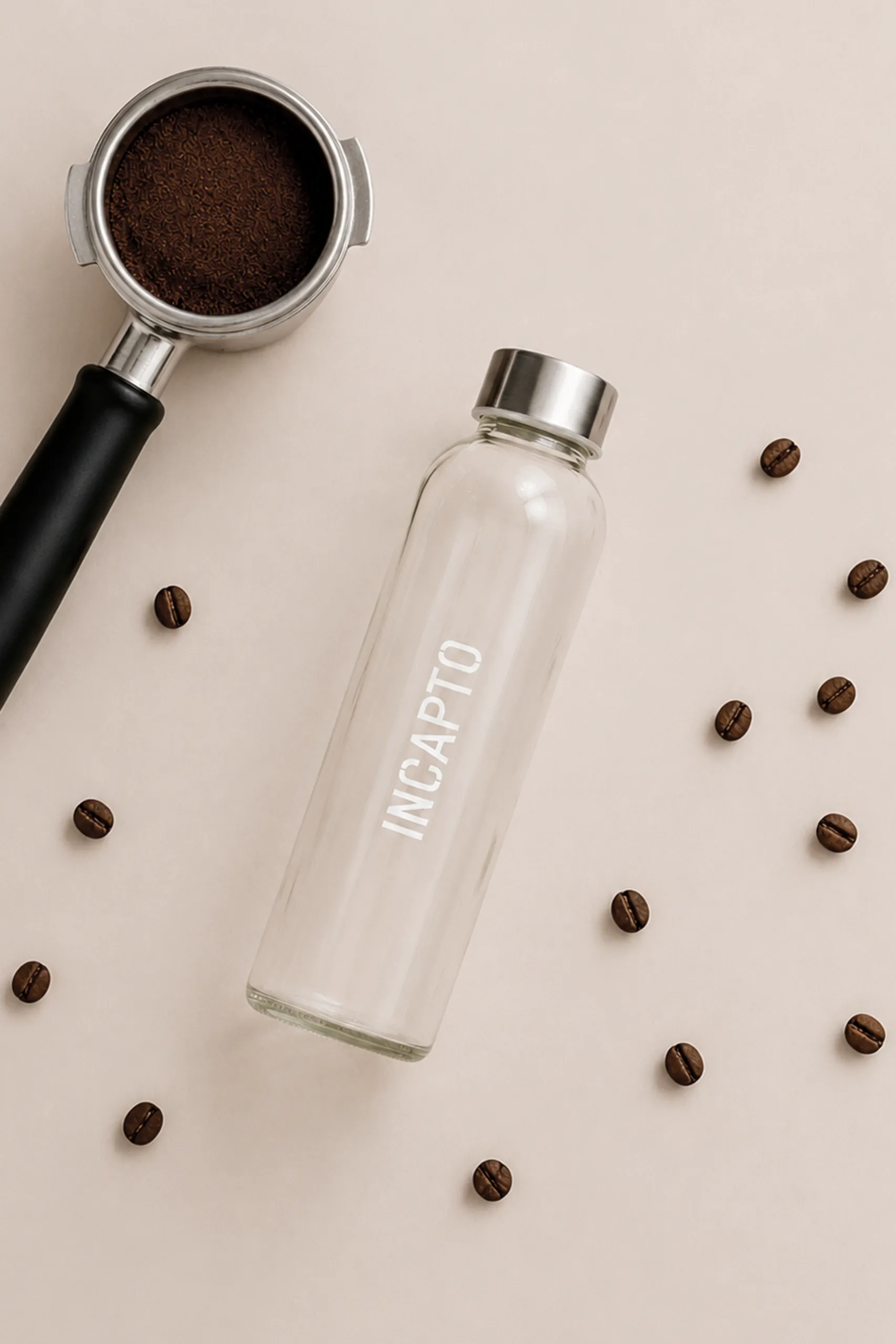 Botella de cristal personalizada para la marca INCAPTO junto a un portafiltro de cafetera con café