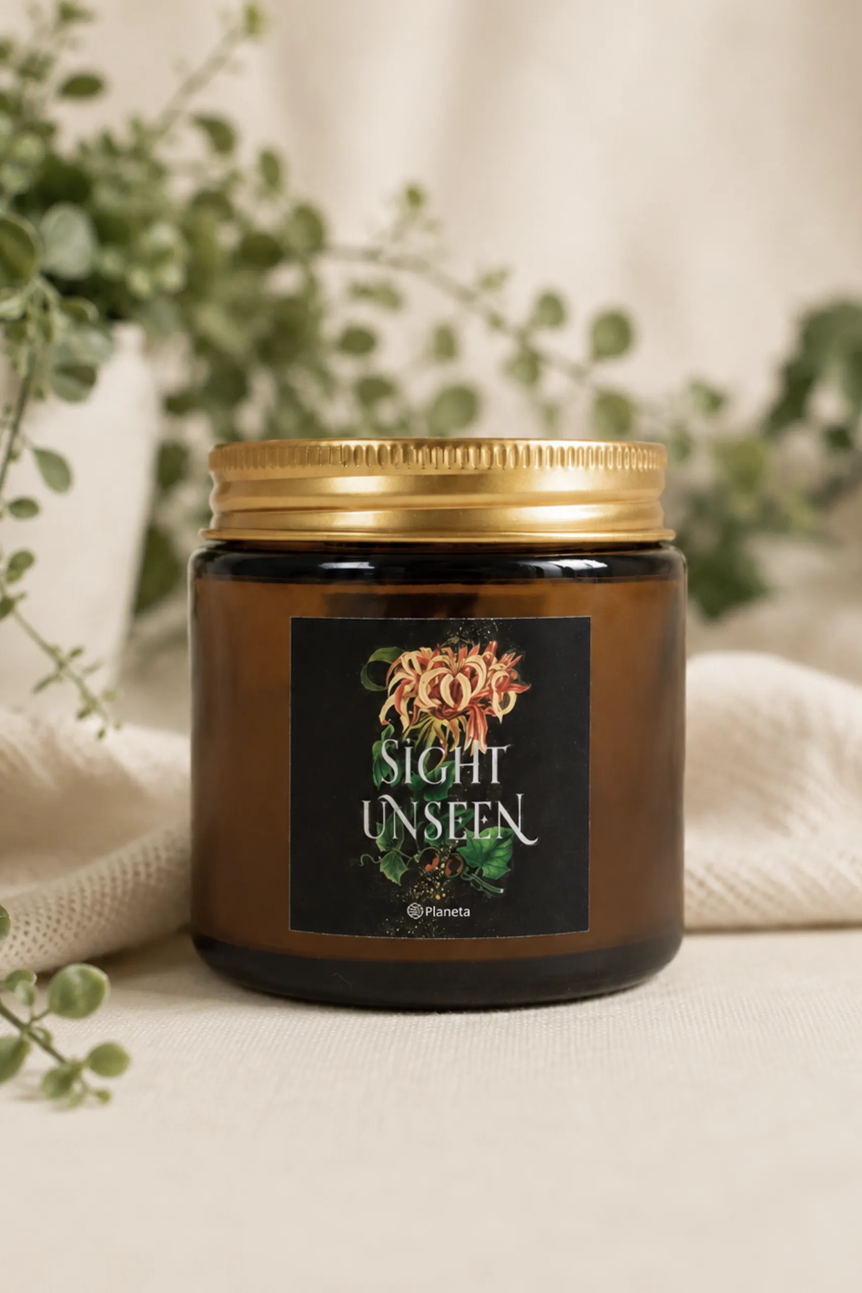 Vela de vidrio marrón con tapa dorada personalizada con la imagen del libro Sight Unseen del Grupo Planeta