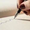 Roller de aluminio reciclado negro con mano escribiendo en cuaderno, personalizado con la palabra LOGO en blanco
