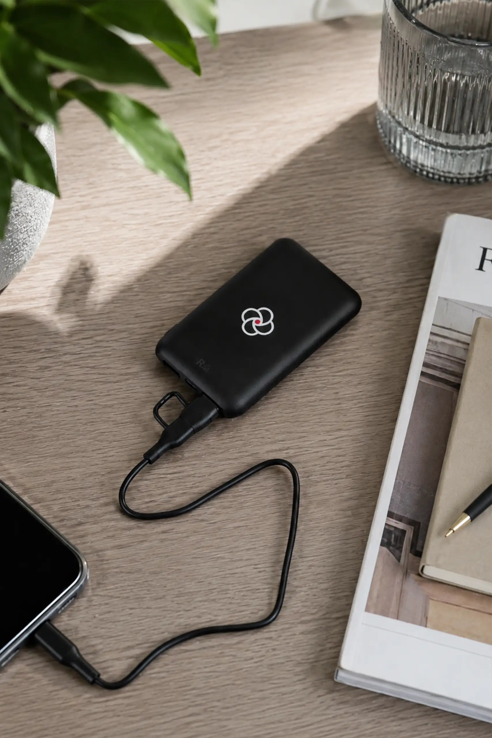 Power bank negro conectado a un móvil sobre una mesa de madera, personalizado con el logo de la empresa MCI