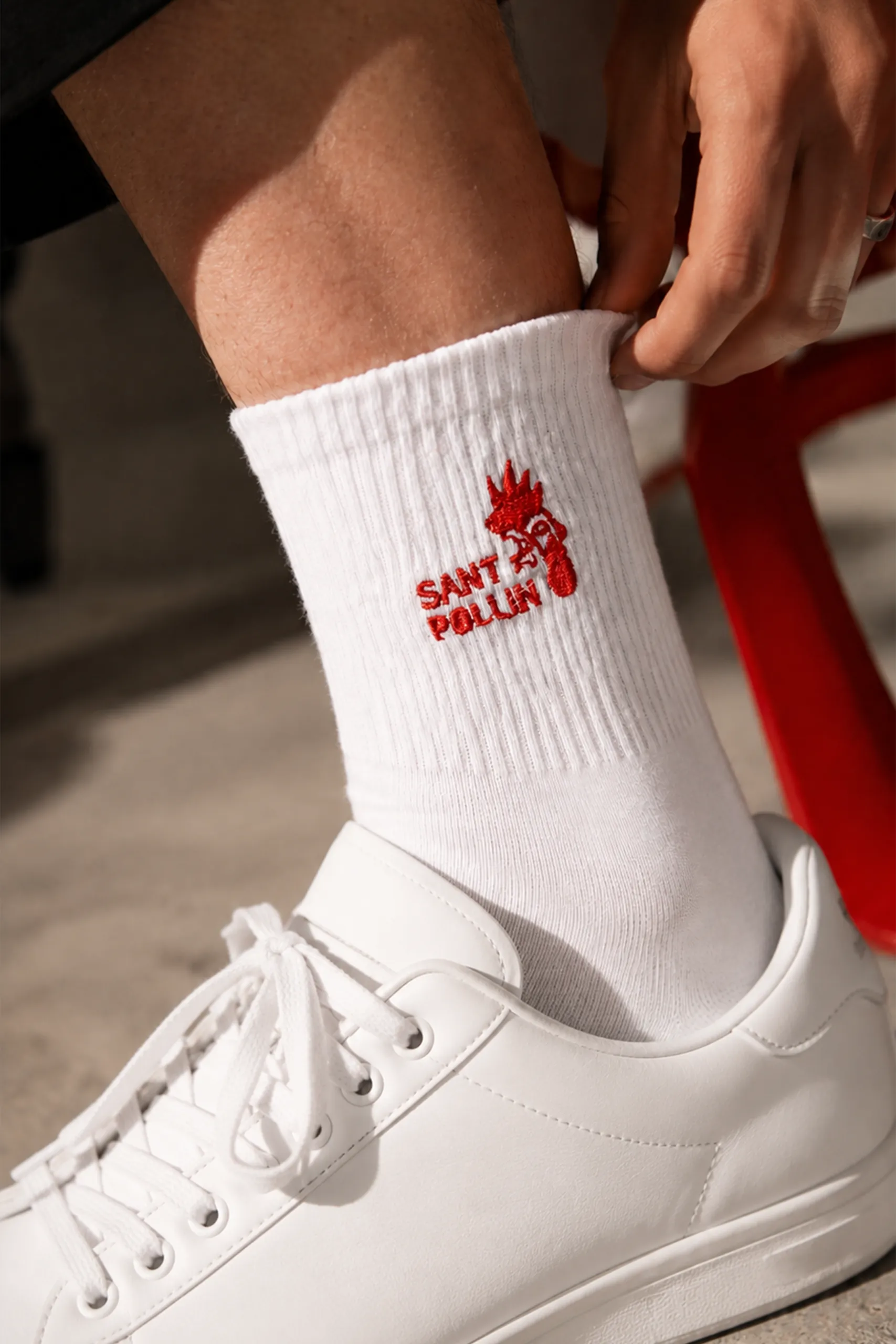 Pie con zapatilla blanca y calcetines blancos personalizados con el logo bordado en rojo de la marca "Sant Pollin"