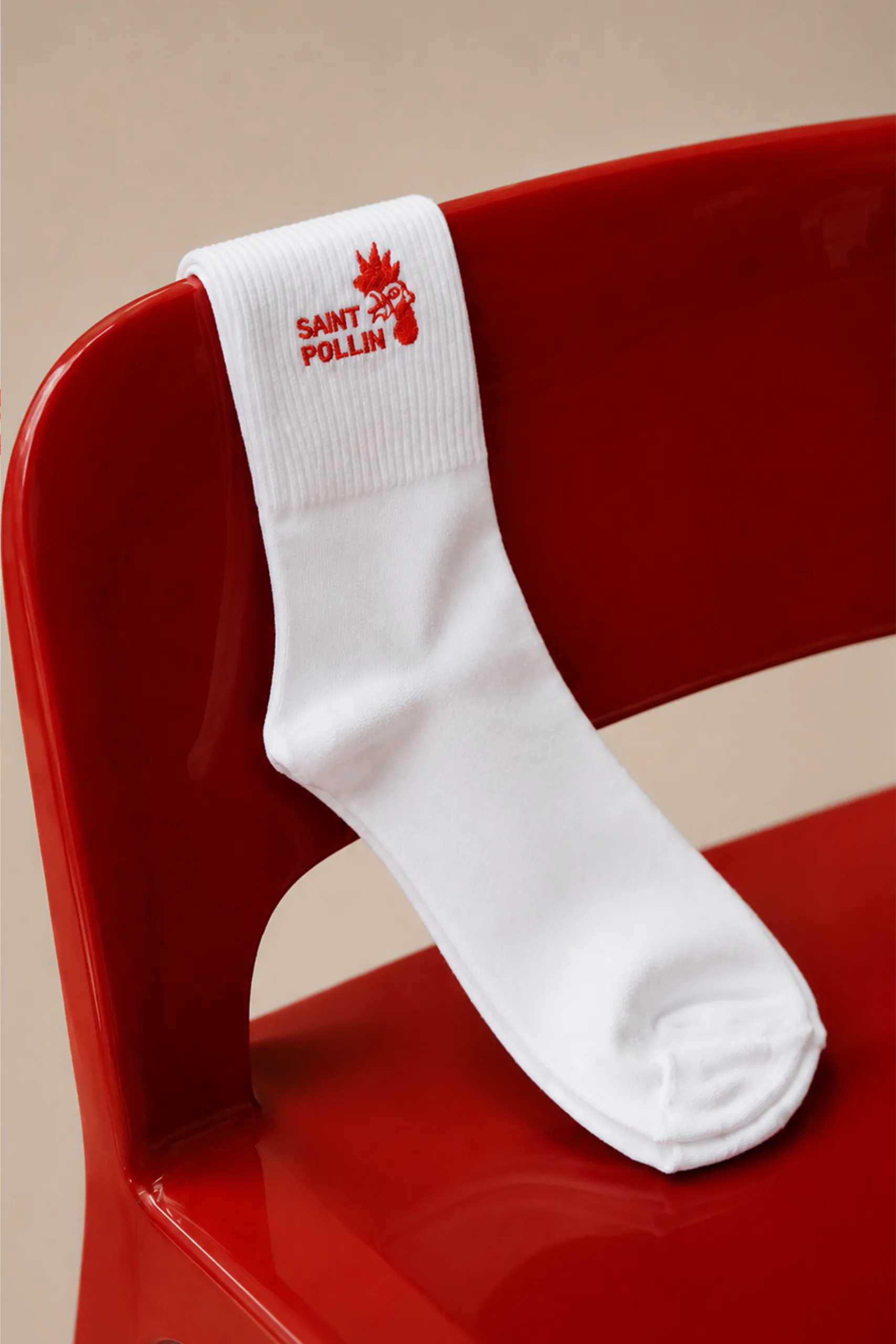 Calcetines blancos personalizados con el logo bordado de la marca "Sant Pollin", colocados sobre una silla roja