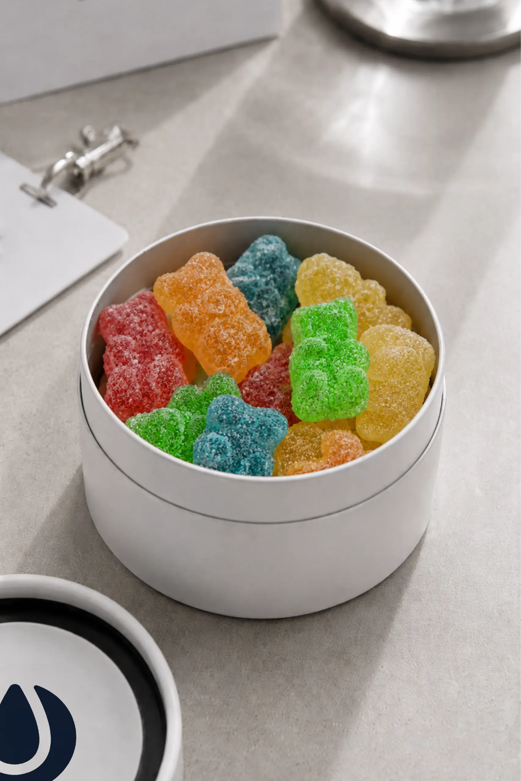 Tarro de cartón con gominolas abierto con impresión a todo color en la tapa circular. En una mesa de oficina.