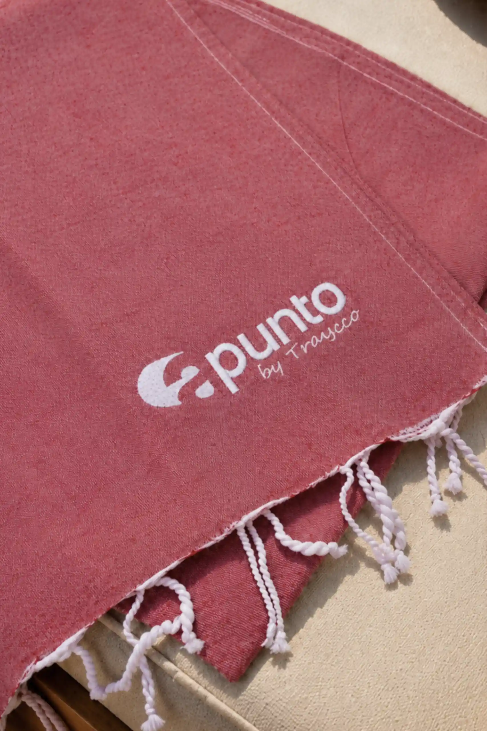 Close-up of the personalised red beach towel featuring the printed Apunto by Traycco logo and white tasselled fringes.