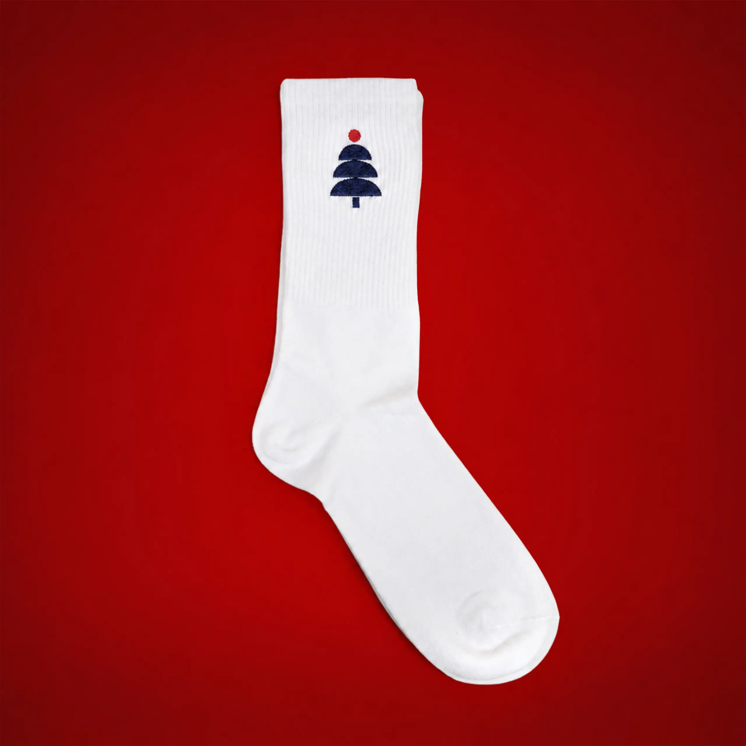 Calcetines bordados_JACKSON Calcetín bordado en blanco con un árbol de Navidad en azul marino y una bola roja, sobre fondo rojo.