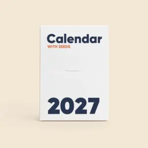 Cardboard case in a white version, showing the cover with the text "Calendar With Seeds 2027" in navy blue and orange, with a perforated opening line across the middle of the box.