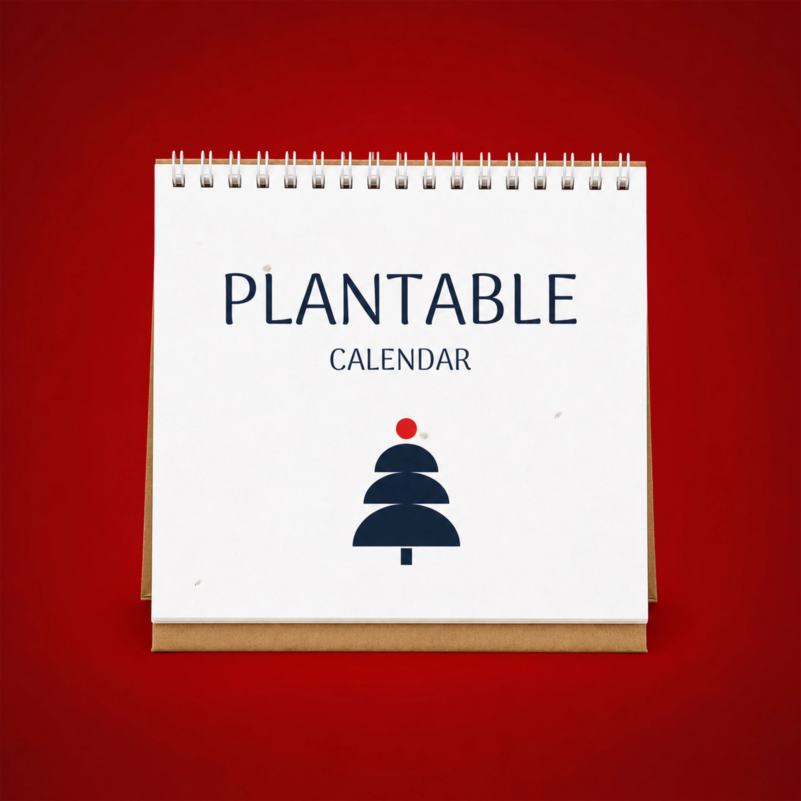 Calendario de mesa con semillas_TRIGA Calendario de mesa plantable con portada que muestra el texto "Plantable Calendar" y un árbol de Navidad estilizado en azul marino con una bola roja, sobre fondo rojo.