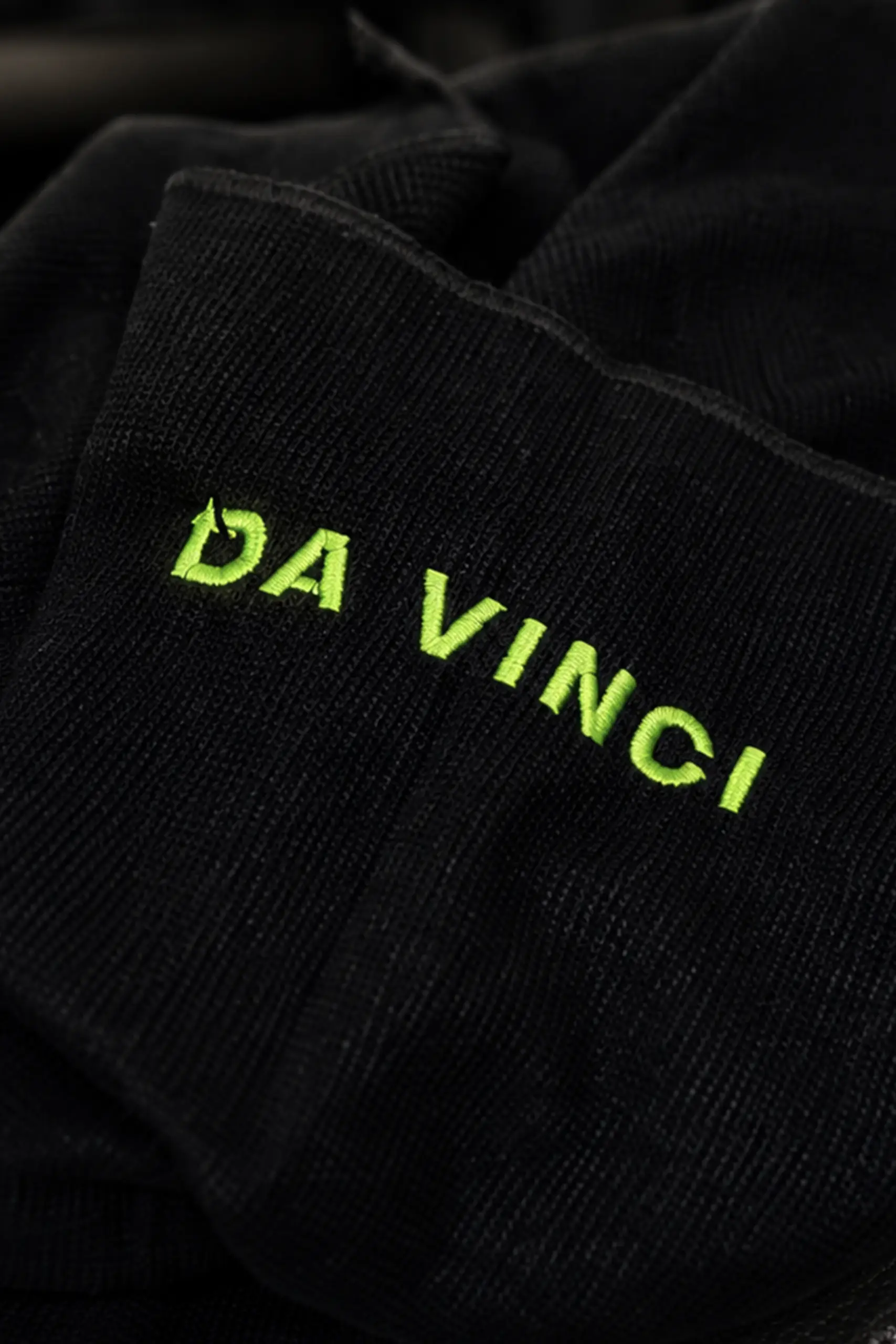 Close-up of a black towel with the "Da Vinci" logo embroidered in lime green on the corner.