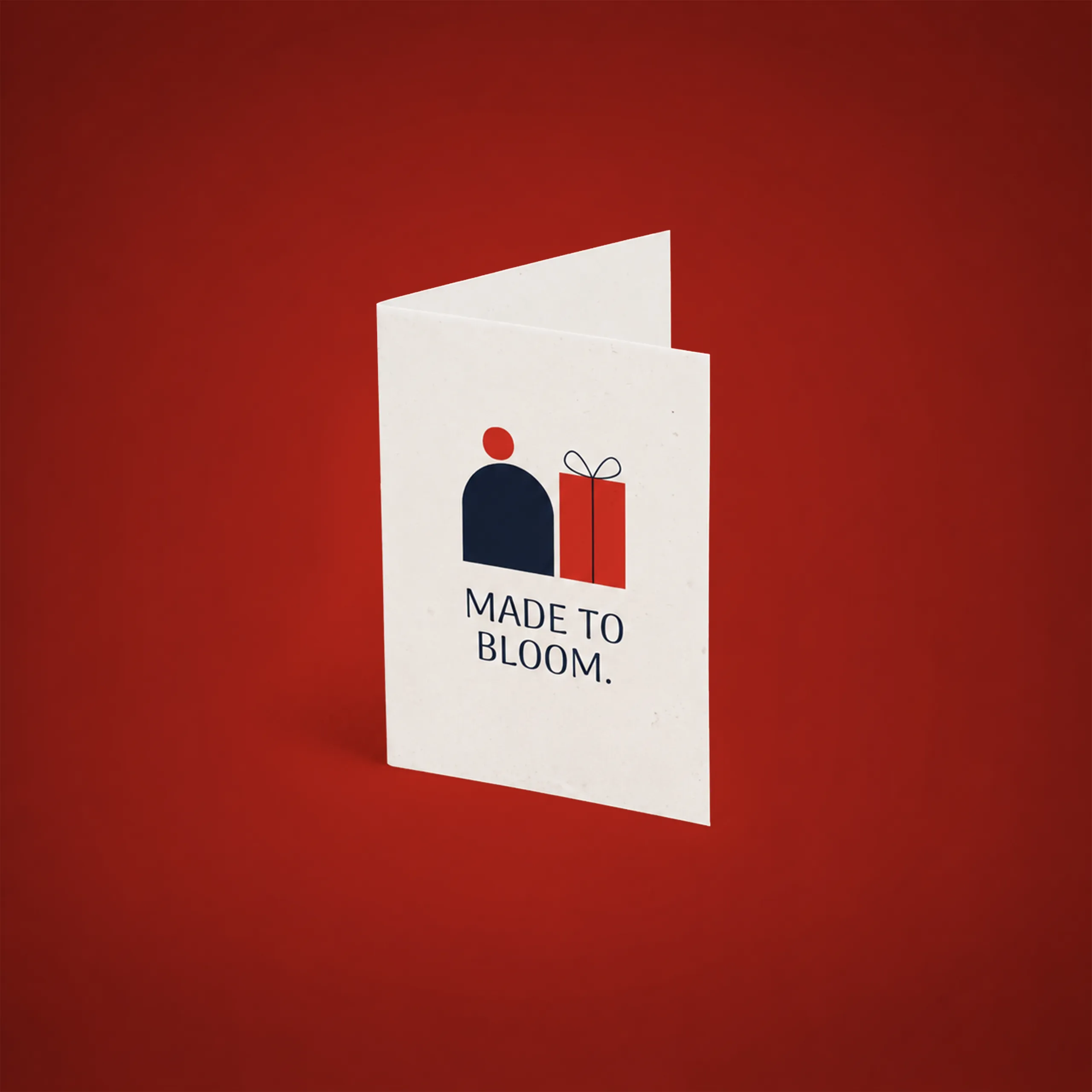 Díptico plantable A6 Díptico plantable en formato A6 abierto en vertical, con una ilustración de una figura y un regalo, y el texto "Made to bloom." sobre fondo rojo.
