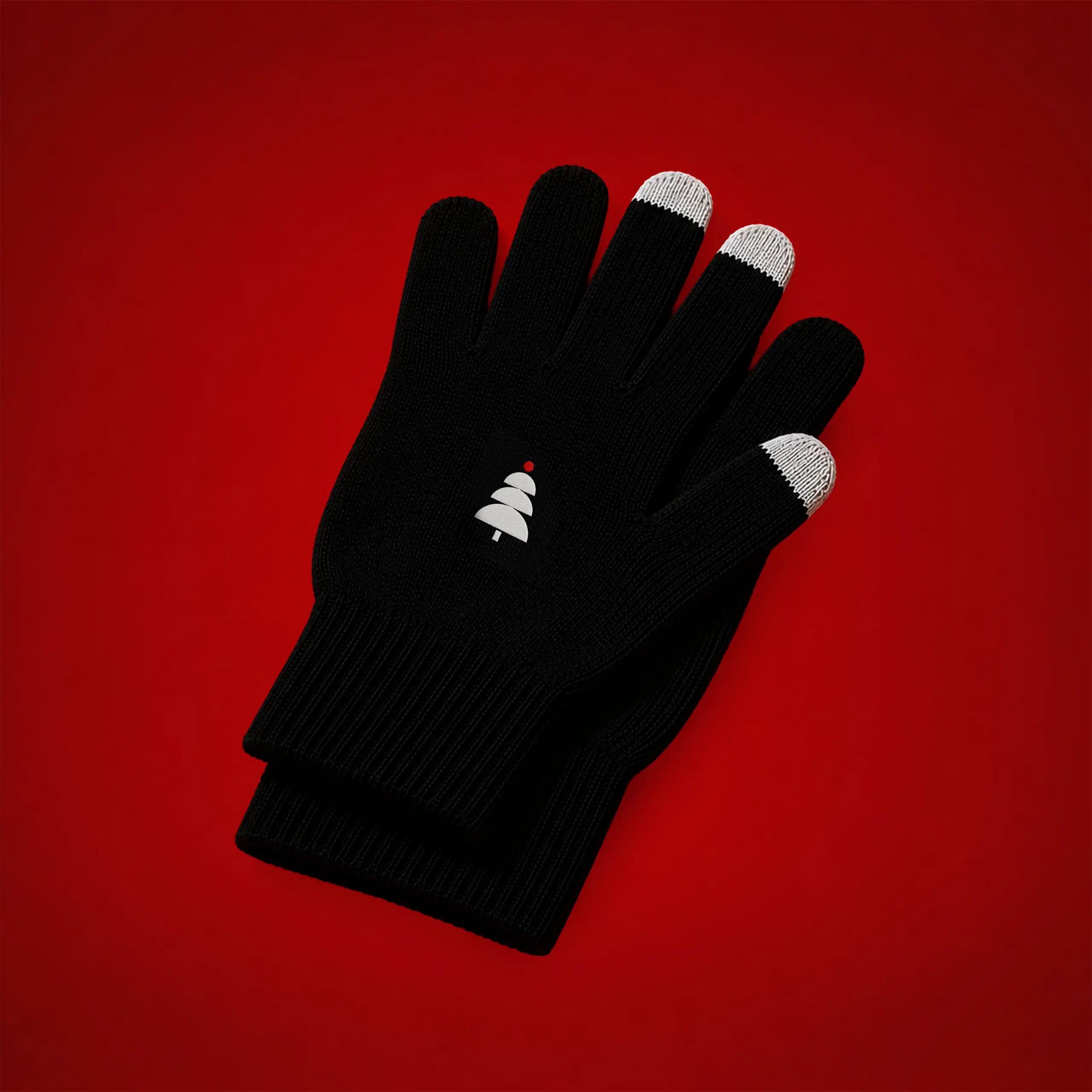 Guantes táctiles ecológicos personalizados_KLEAN Par de guantes táctiles ecológicos en color negro con las puntas de los dedos índice y corazón en blanco para uso con pantallas táctiles, y un árbol de Navidad bordado en blanco con una bola roja, sobre fondo rojo.