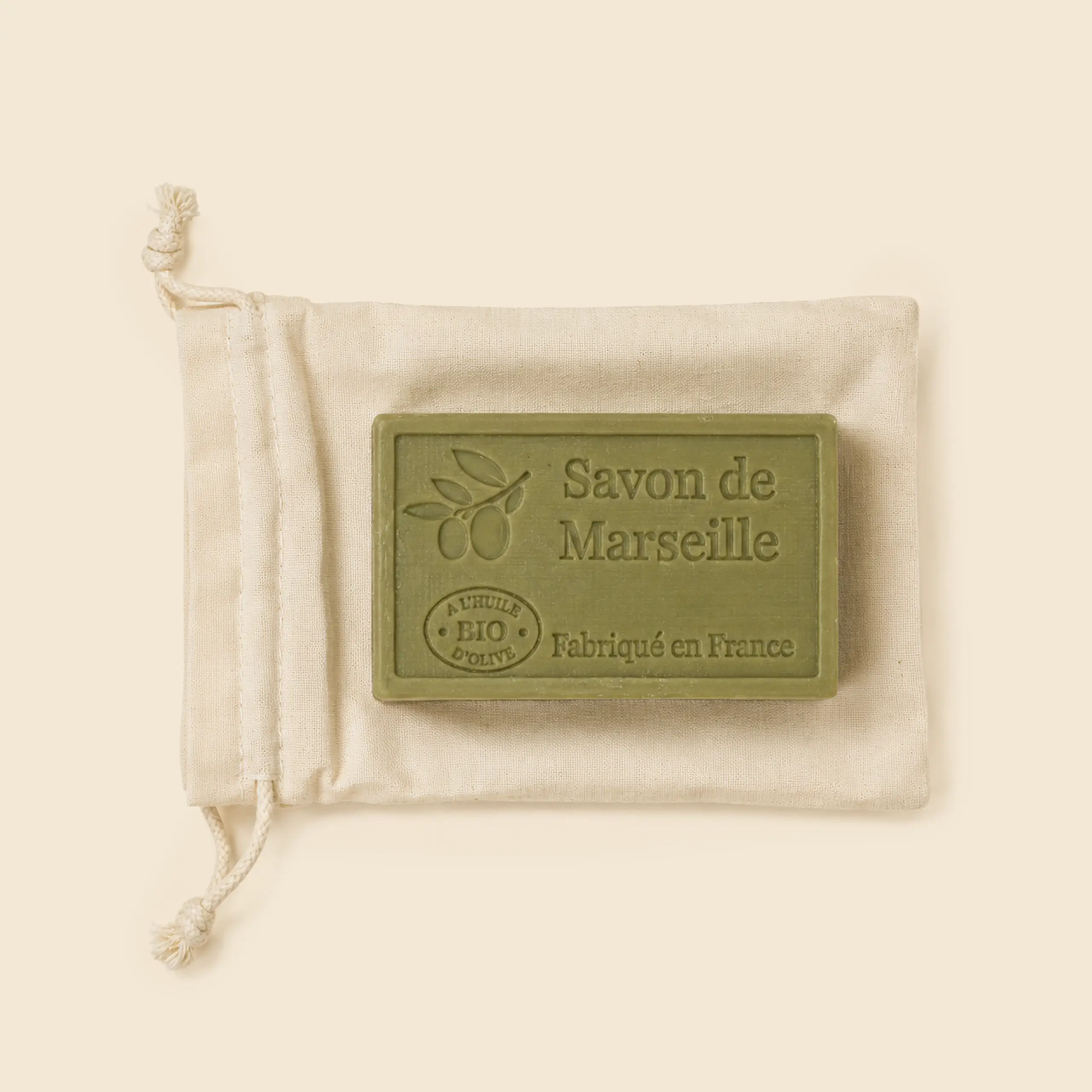 Jabón de Marsella con aceite de oliva bio sobre bolsa de algodón personalizable, fabricado en Francia, fondo beige.
