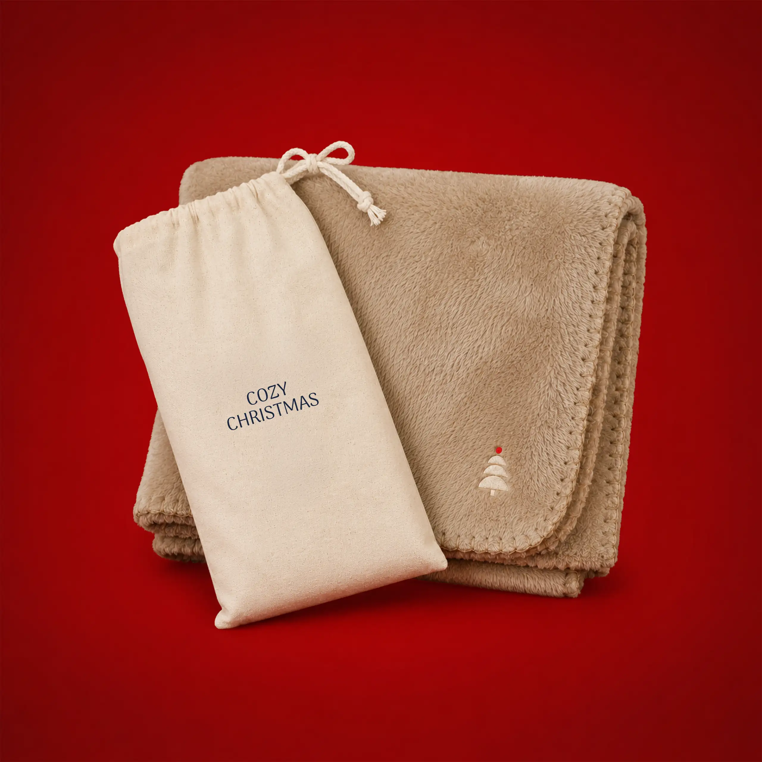 Manta ecológica personalizada de 200 g_m2_SERENA Manta ecológica personalizada en color beige, doblada junto a su funda de tela a juego con el texto "Cozy Christmas" y un pequeño árbol de Navidad bordado, sobre fondo rojo.