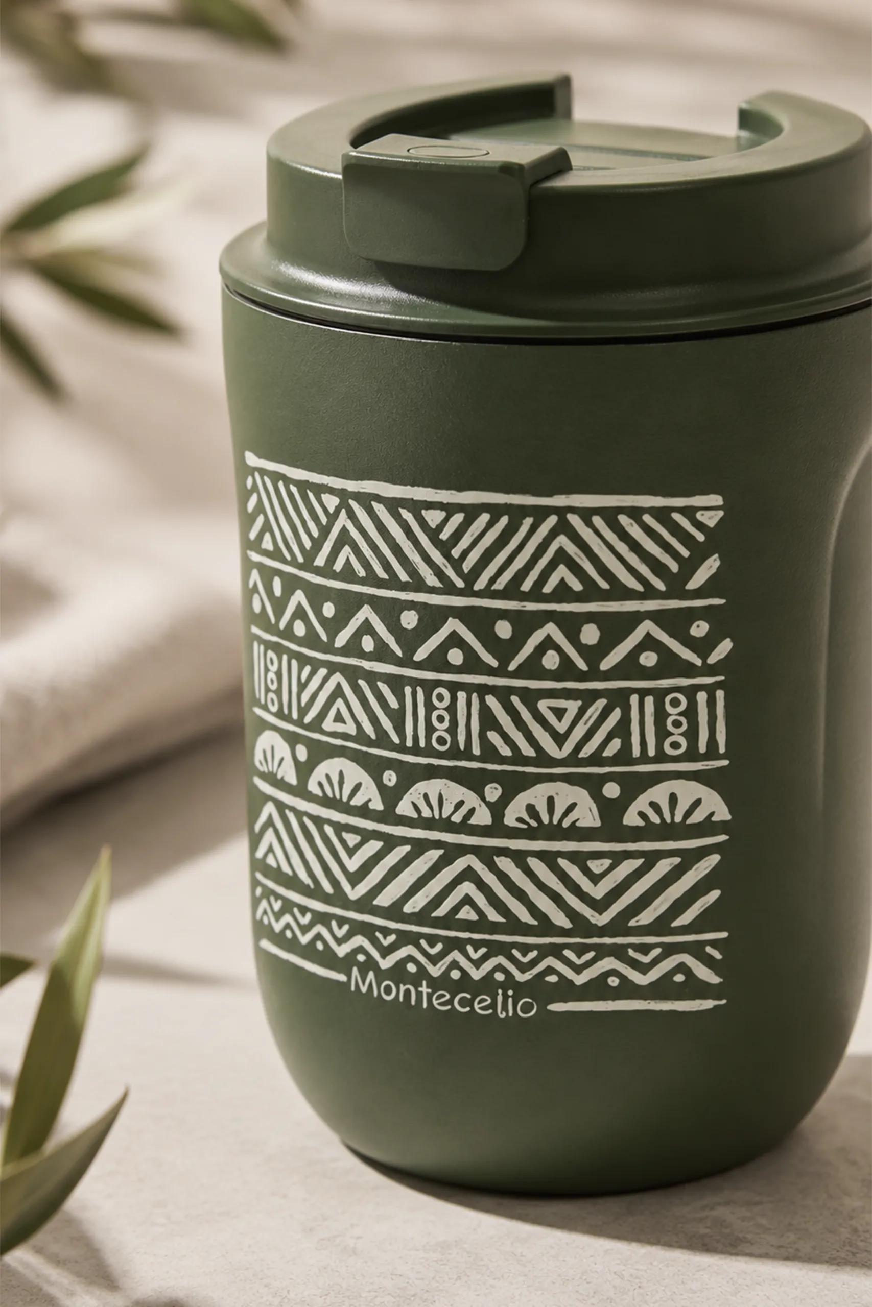 Gros plan sur un gobelet thermique vert olive portant le texte « Montecelio » imprimé, montrant en détail le motif géométrique ethnique blanc et le couvercle assorti.