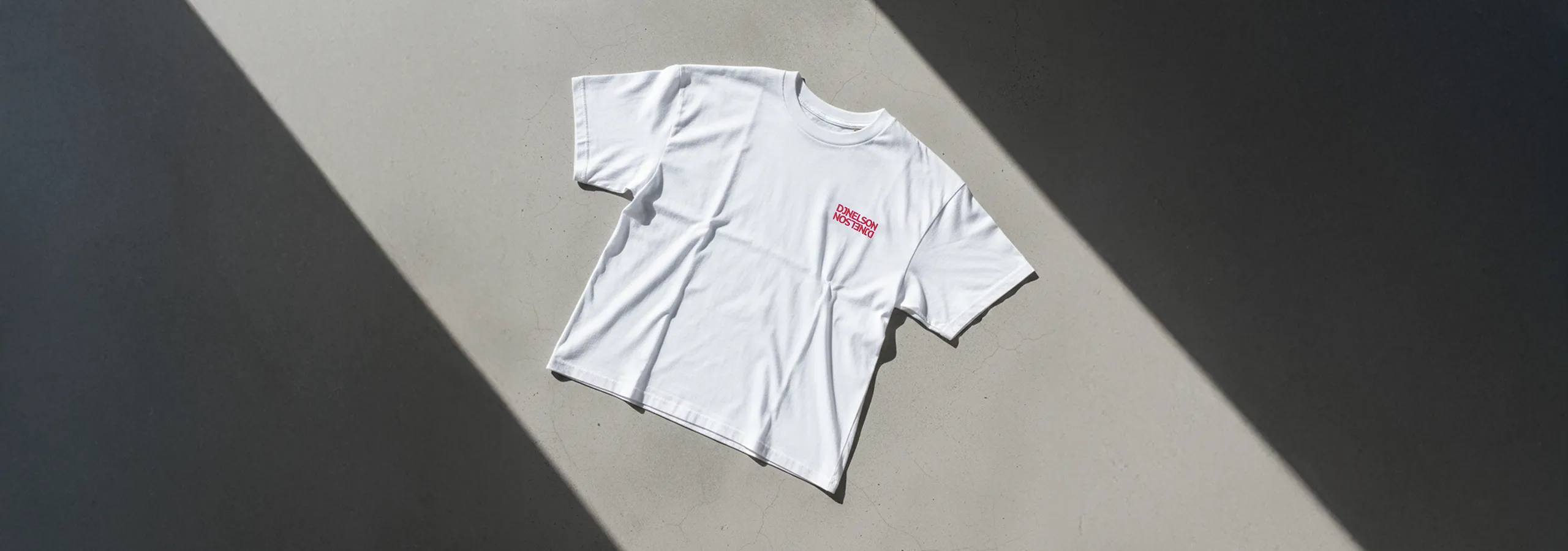 Camiseta blanca con bordado colocada en un suelo de cemento.