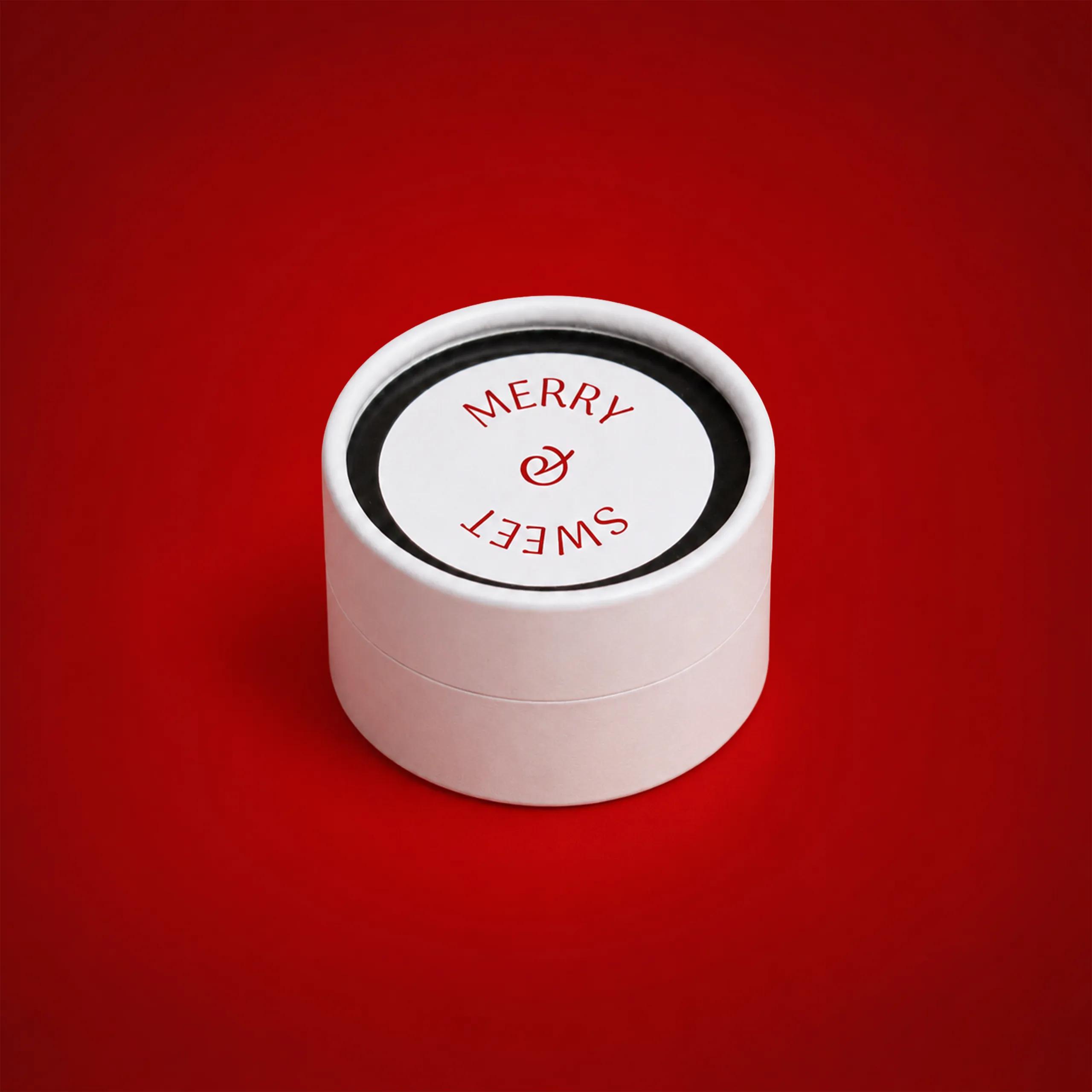 Tarro de cartón personalizado con gominolas_LOLLY Tarro de cartón personalizado en color rosa pálido con tapa mostrando el texto "Merry Sweet" en rojo y un logo estilizado, sobre fondo rojo.
