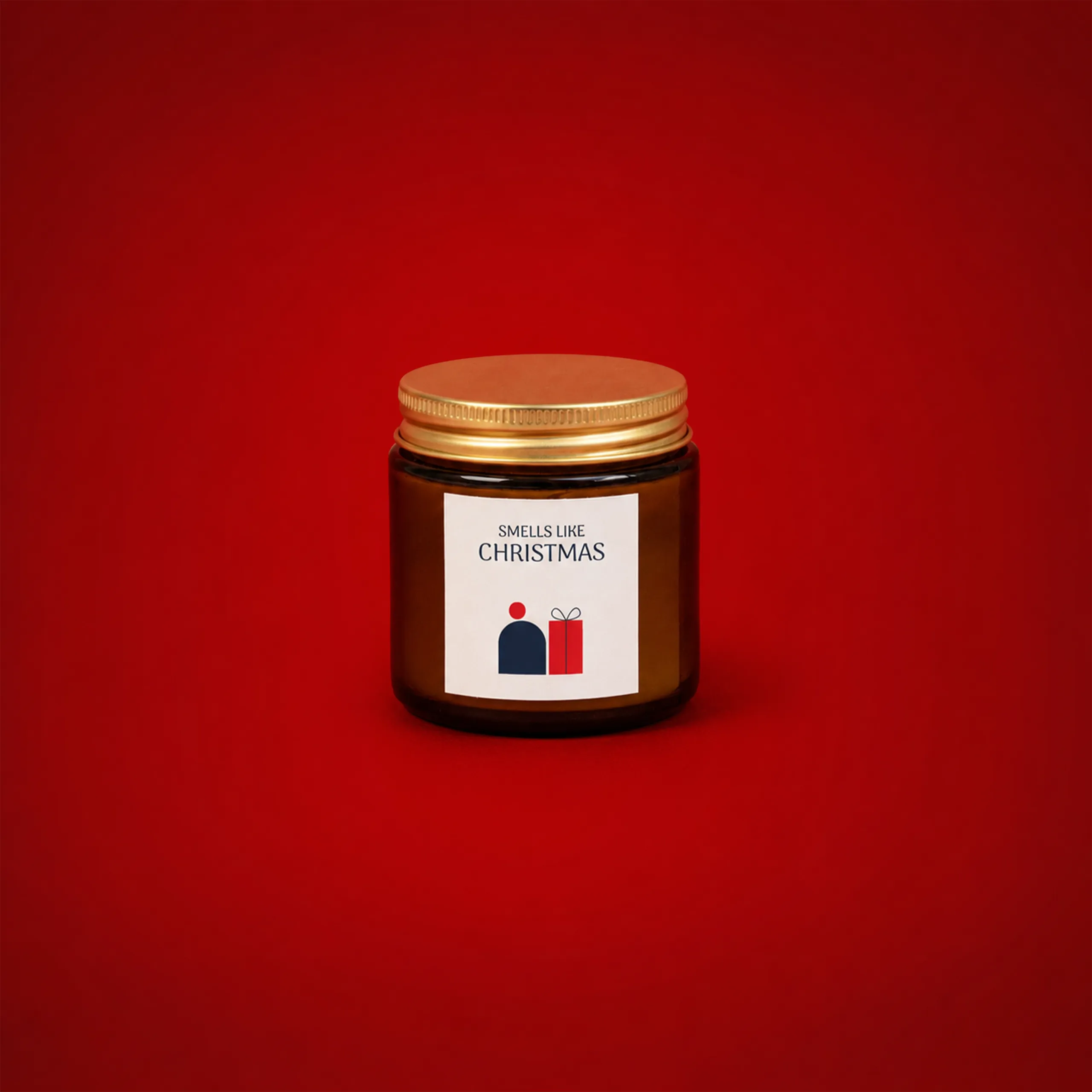 Vela aromática personalizada_VERA Vela aromática personalizada en tarro ámbar con tapa dorada, etiqueta blanca con el texto "Smells like Christmas" y una ilustración de una figura junto a un regalo, sobre fondo rojo.