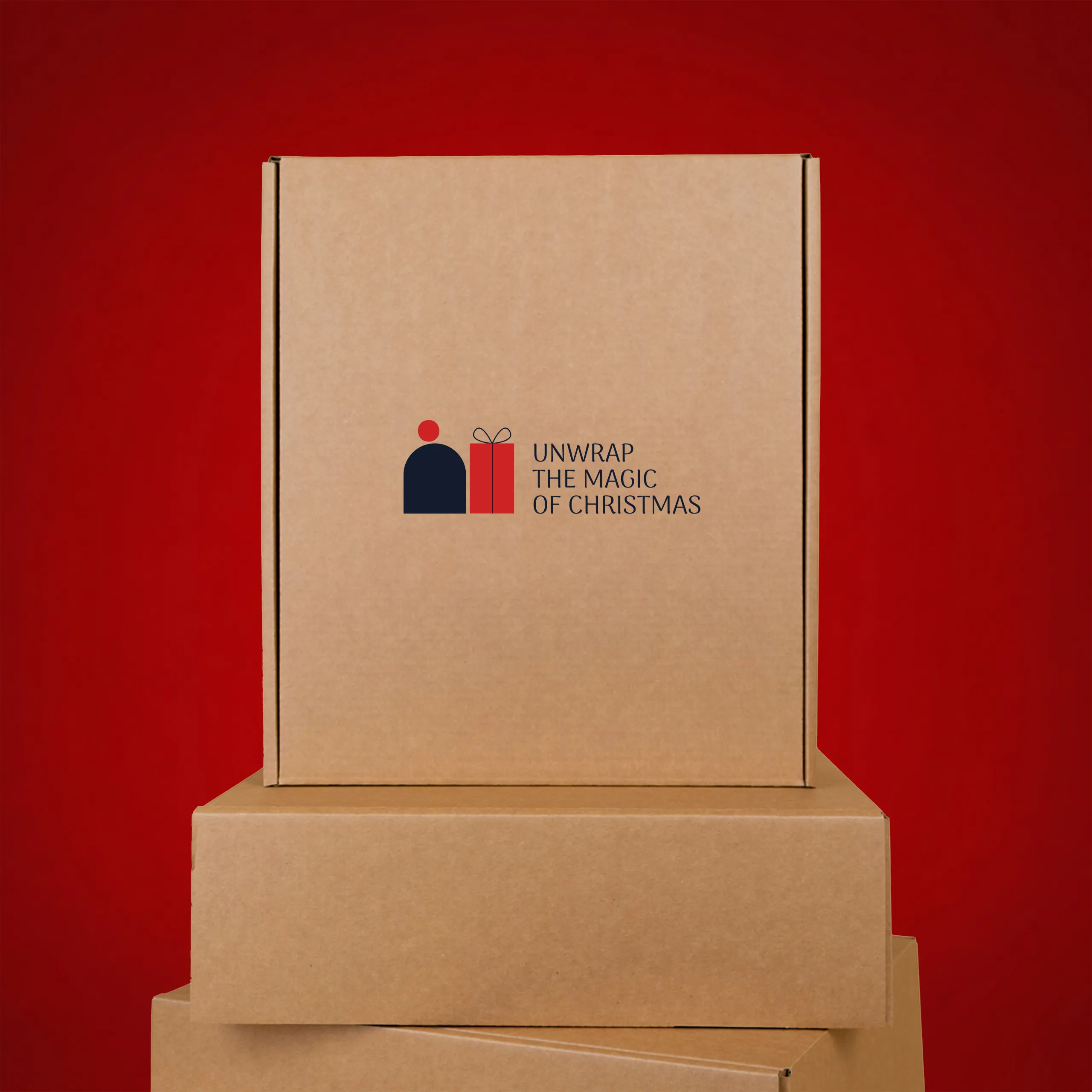 Eco-friendly kraft cardboard box in a tall, upright format, stacked on top of other boxes, printed with the "Unwrap the magic of Christmas" logo in navy blue and red, against a red background.
