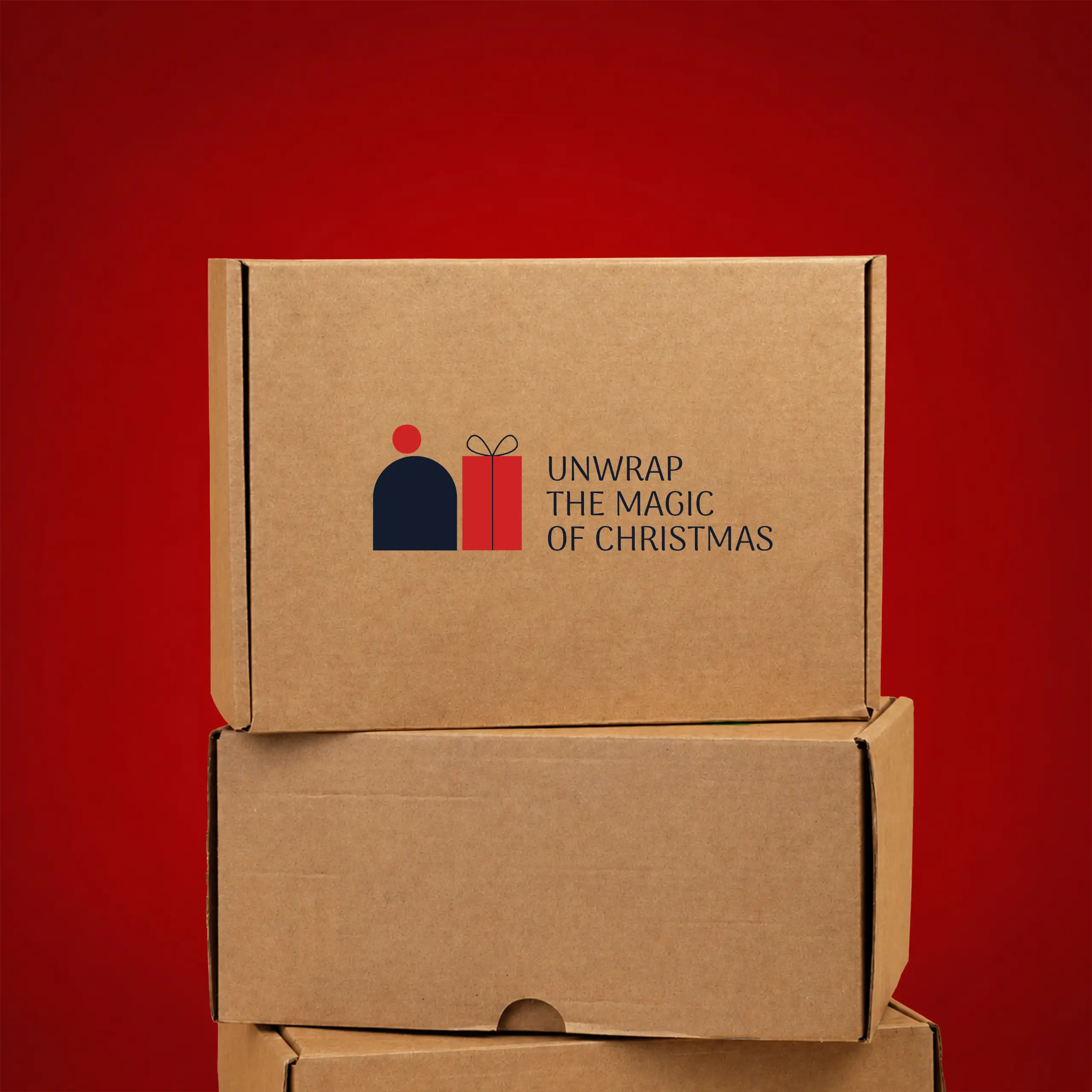 Eco-friendly kraft cardboard box in a wider, more compact horizontal format, stacked on top of other boxes, printed with the "Unwrap the magic of Christmas" logo in navy blue and red, against a red background.