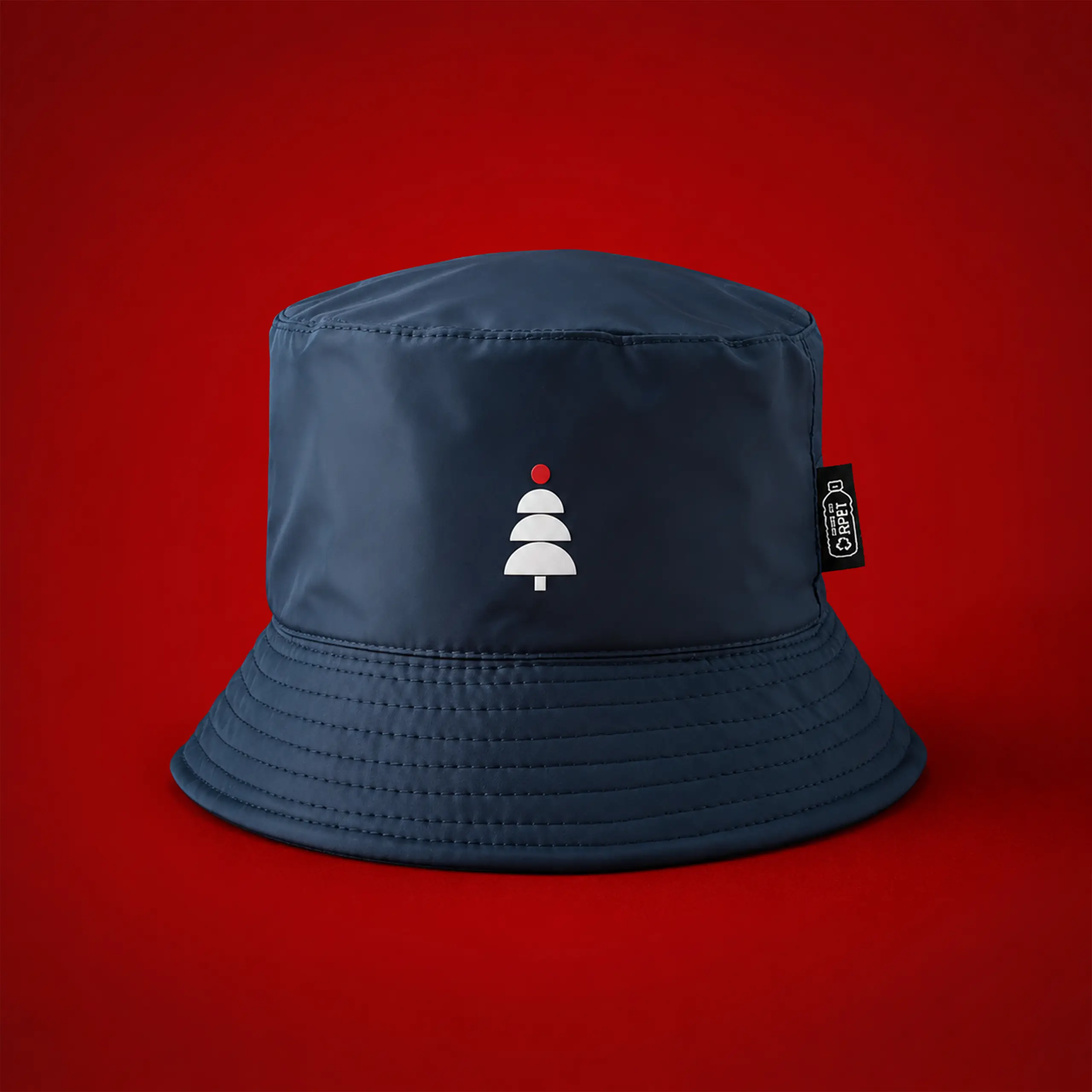 Gorro impermeable reversible TWIST Gorro de pescador (bucket hat) impermeable en color azul marino, fabricado en tejido RPET reciclado, con un pequeño árbol de Navidad bordado en blanco y rojo sobre fondo rojo.