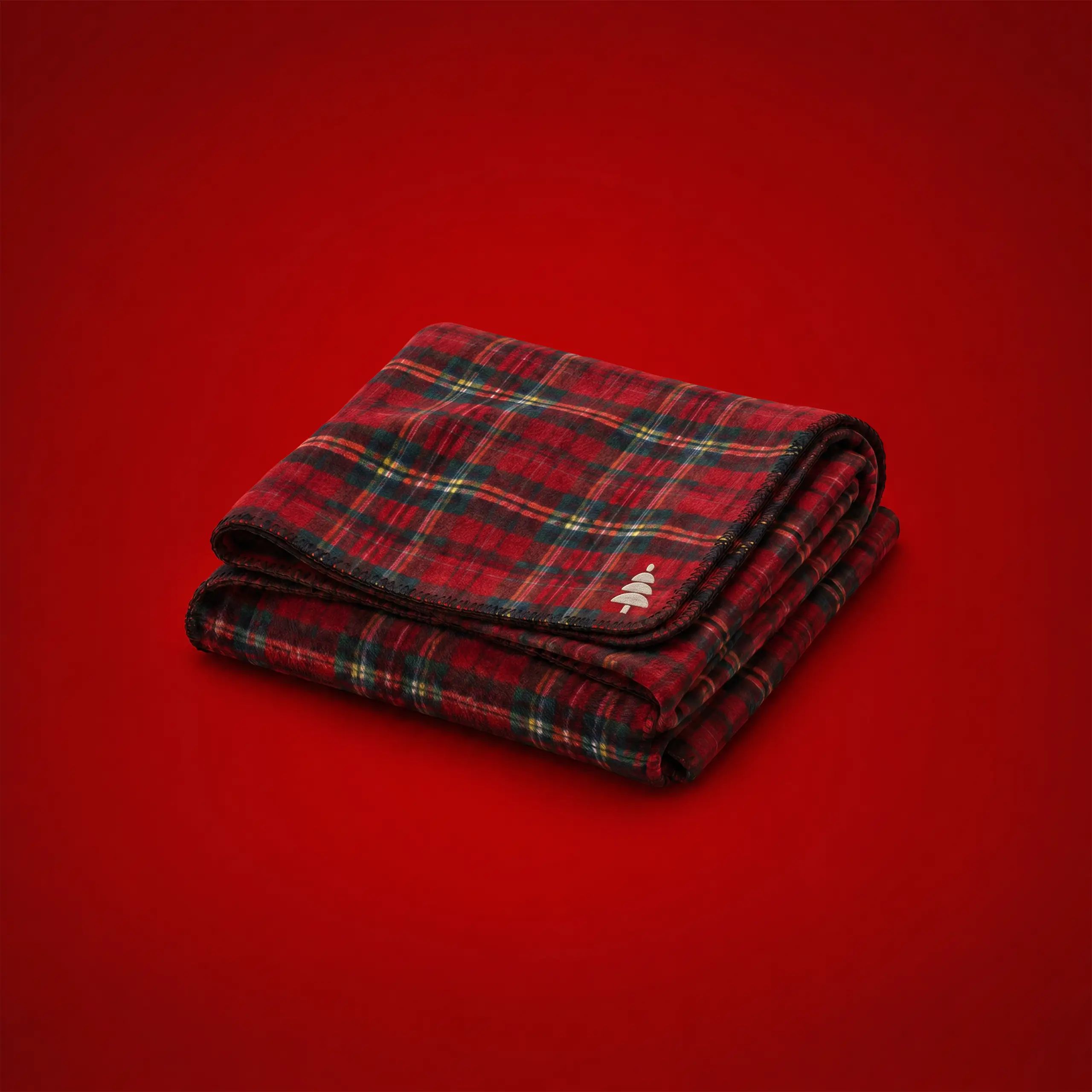 Red, green and gold tartan fleece blanket, folded on a festive red background, with a Christmas tree icon embroidered in the corner.