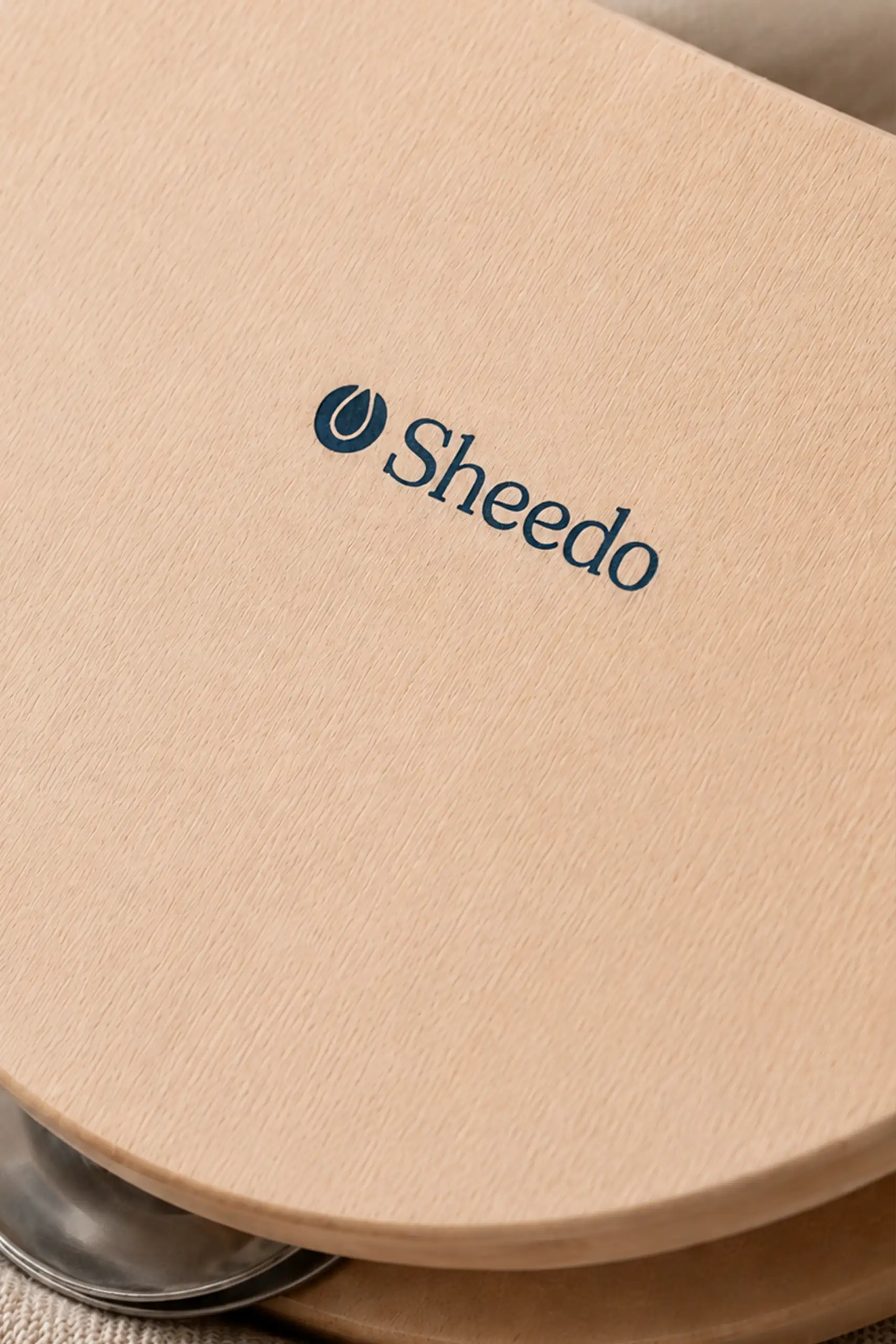 Primer plano del logotipo "Sheedo" grabado en la madera clara de la pandereta, mostrando el detalle y el grano de la madera.