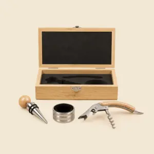 Caja de bambú abierta con set de accesorios para vino sobre fondo beige, mostrando el interior acolchado en negro con hueco para el tapón, el anillo antigoteo y el sacacorchos.