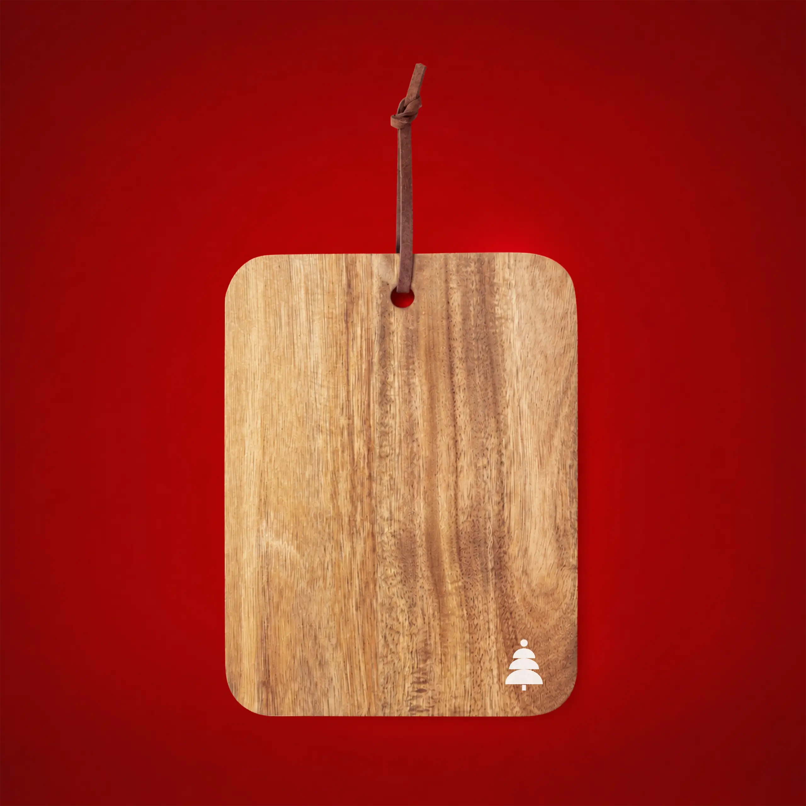 Personalised wooden cutting board hanging by a leather cord on a festive red background, with a Christmas tree icon engraved in the corner.
