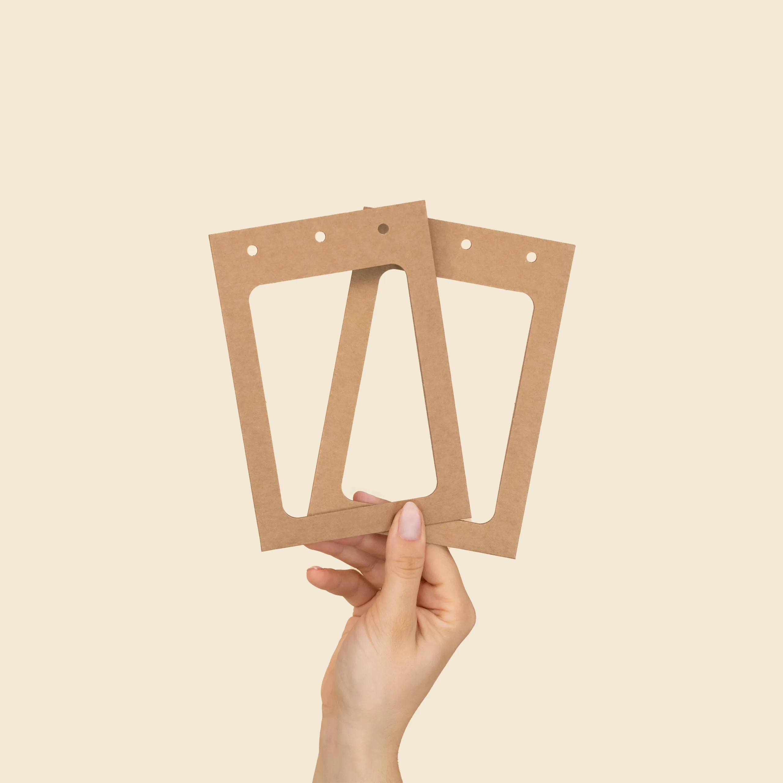 Funda KASE 0/0 - 12,2x8,1 - Ventana Doble Mano sujetando dos fundas de acreditación A6 de cartón kraft abiertas en abanico, mostrando la ventana y los tres perforados.
